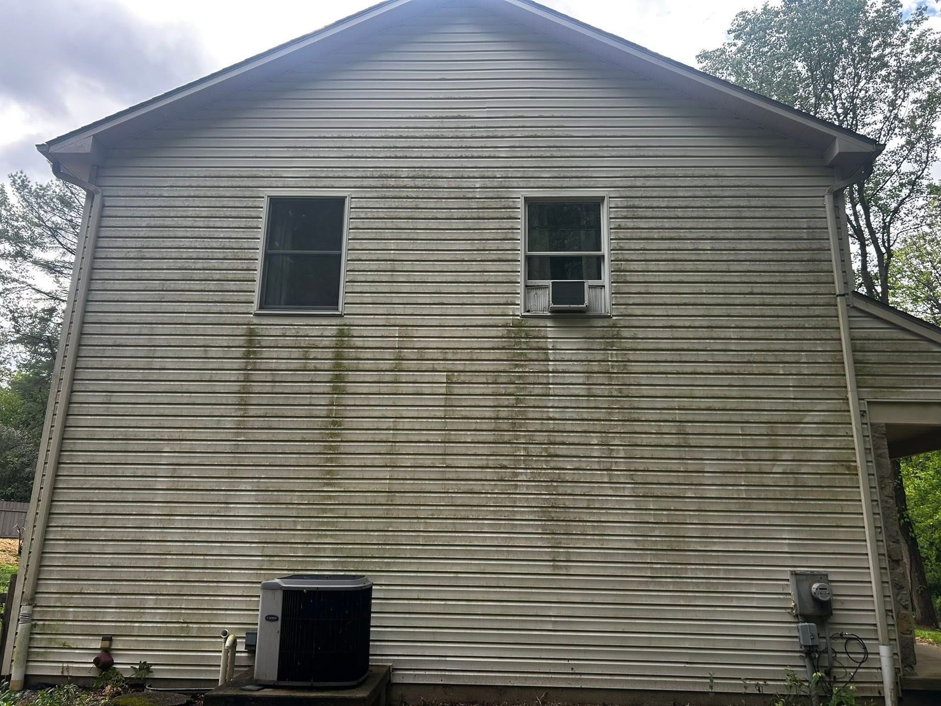 Person pressure-washing a gray house siding with a long nozzle