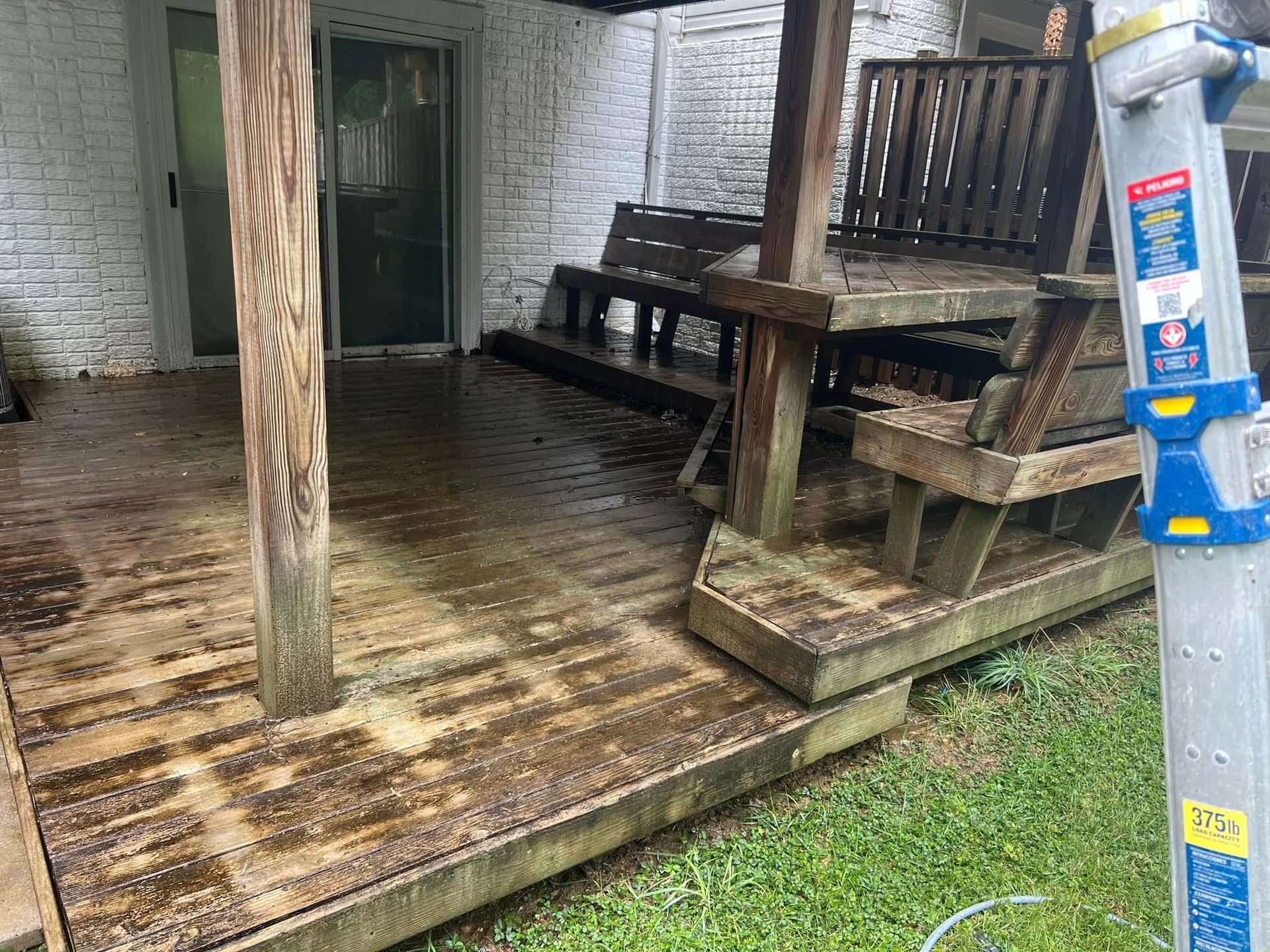 Person pressure-washing wooden deck with a spray wand, water splashing across the planks
