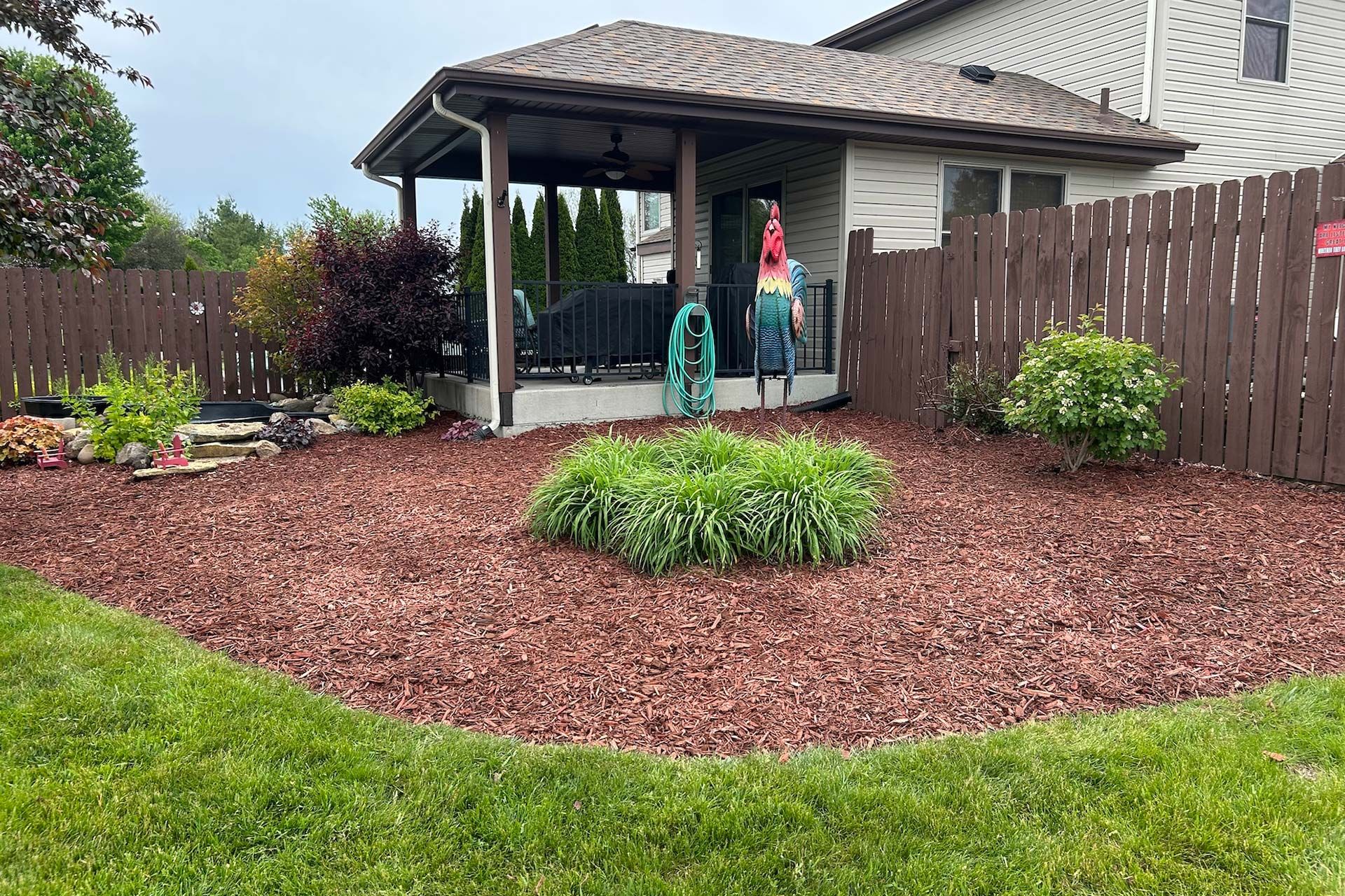 Backyard patio with covered seating, red mulch beds, and green lawn after landscaping