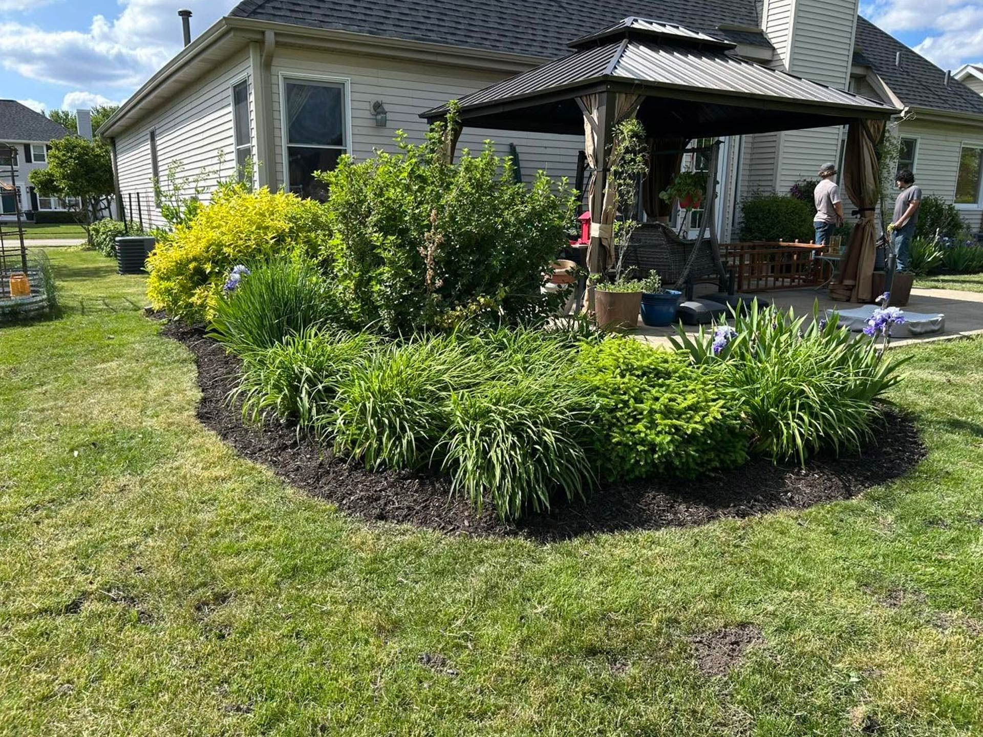 Backyard patio with a gazebo, potted plants, and a curved flower bed beside a house