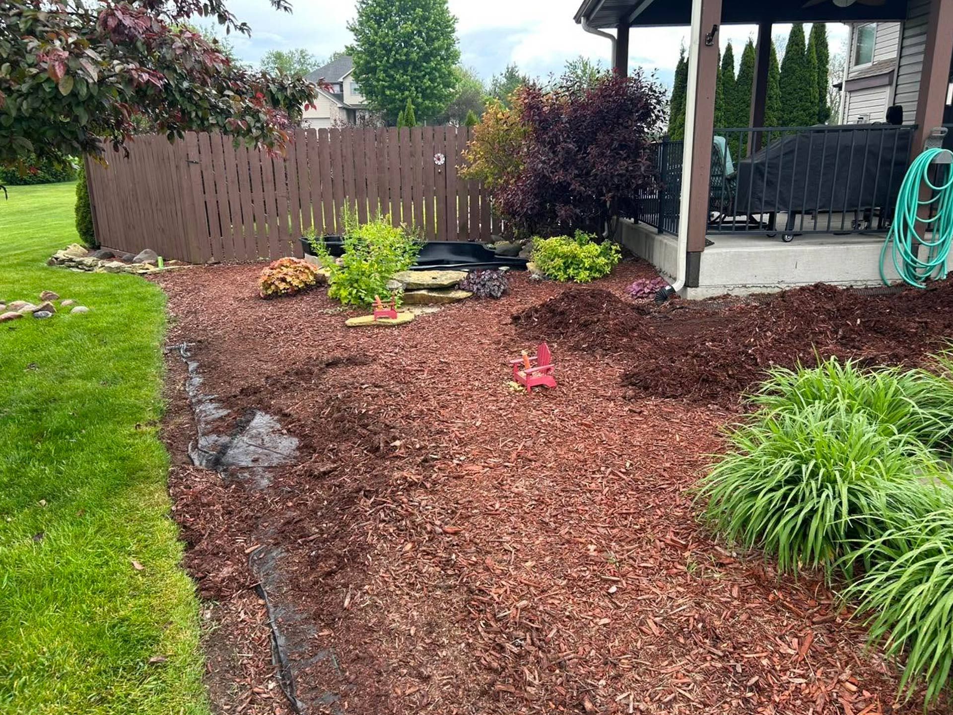 Backyard garden with fresh mulch, plants, a wooden fence, and a covered patio.