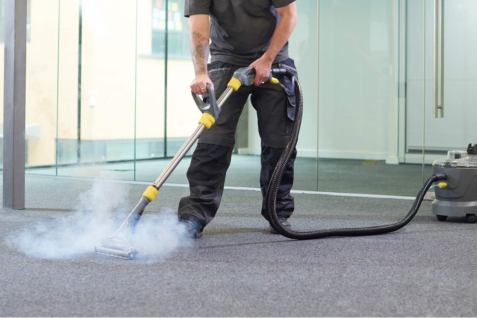 Person pressure-washing a carpeted floor indoors, with a hose and spray of water.