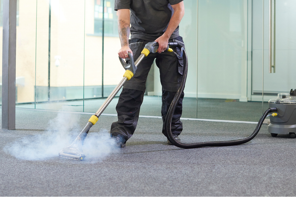 Person pressure-washing a carpeted floor indoors, with a hose and spray of water.