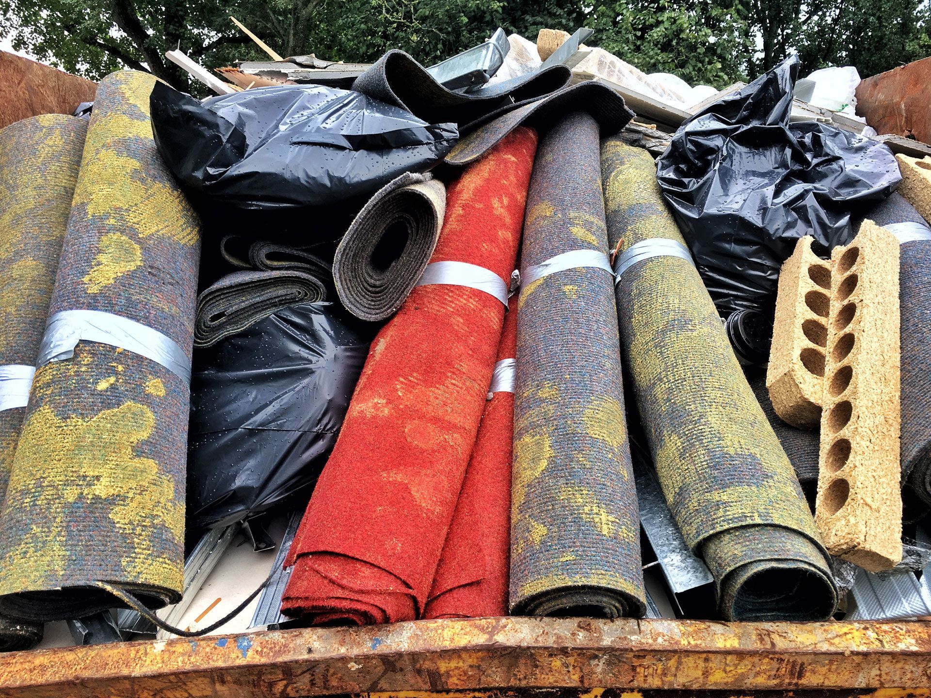 Pile of rolled roofing materials and tarps in black, red, and gray, with a cinder block on the right