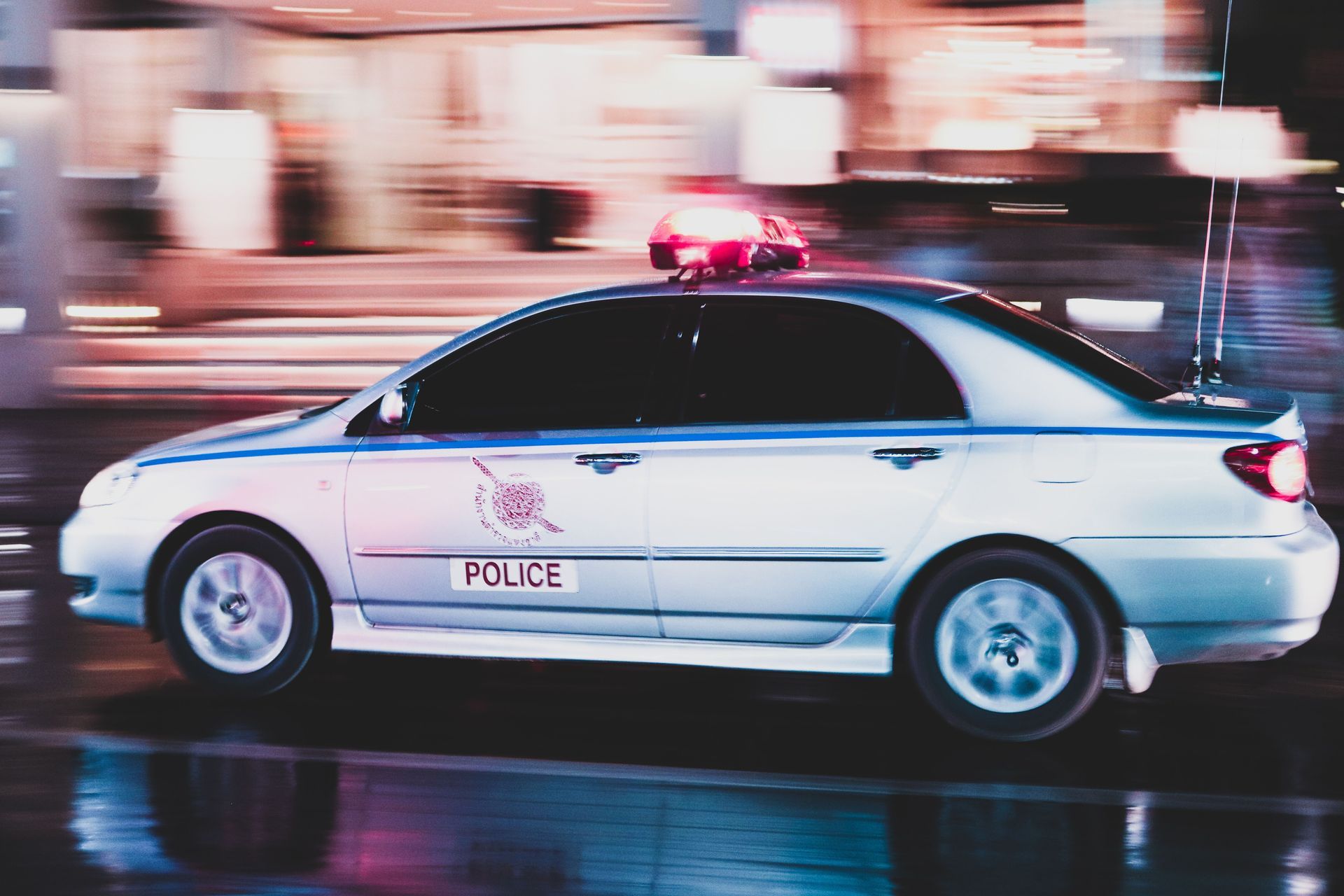 White police sedan with flashing red lights driving at night on a city street
