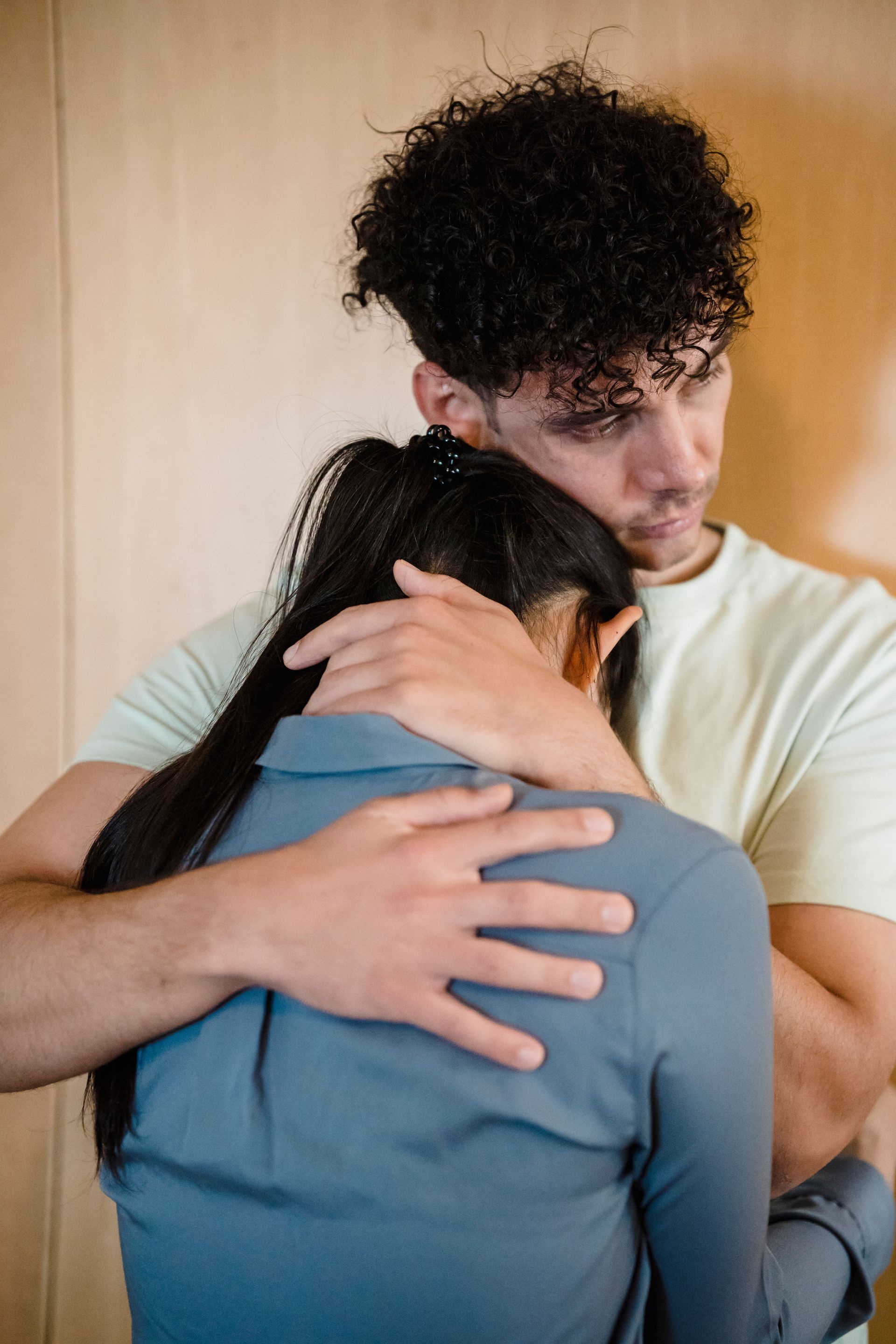 Two people embracing closely indoors, one comforting the other with a hand on their back.