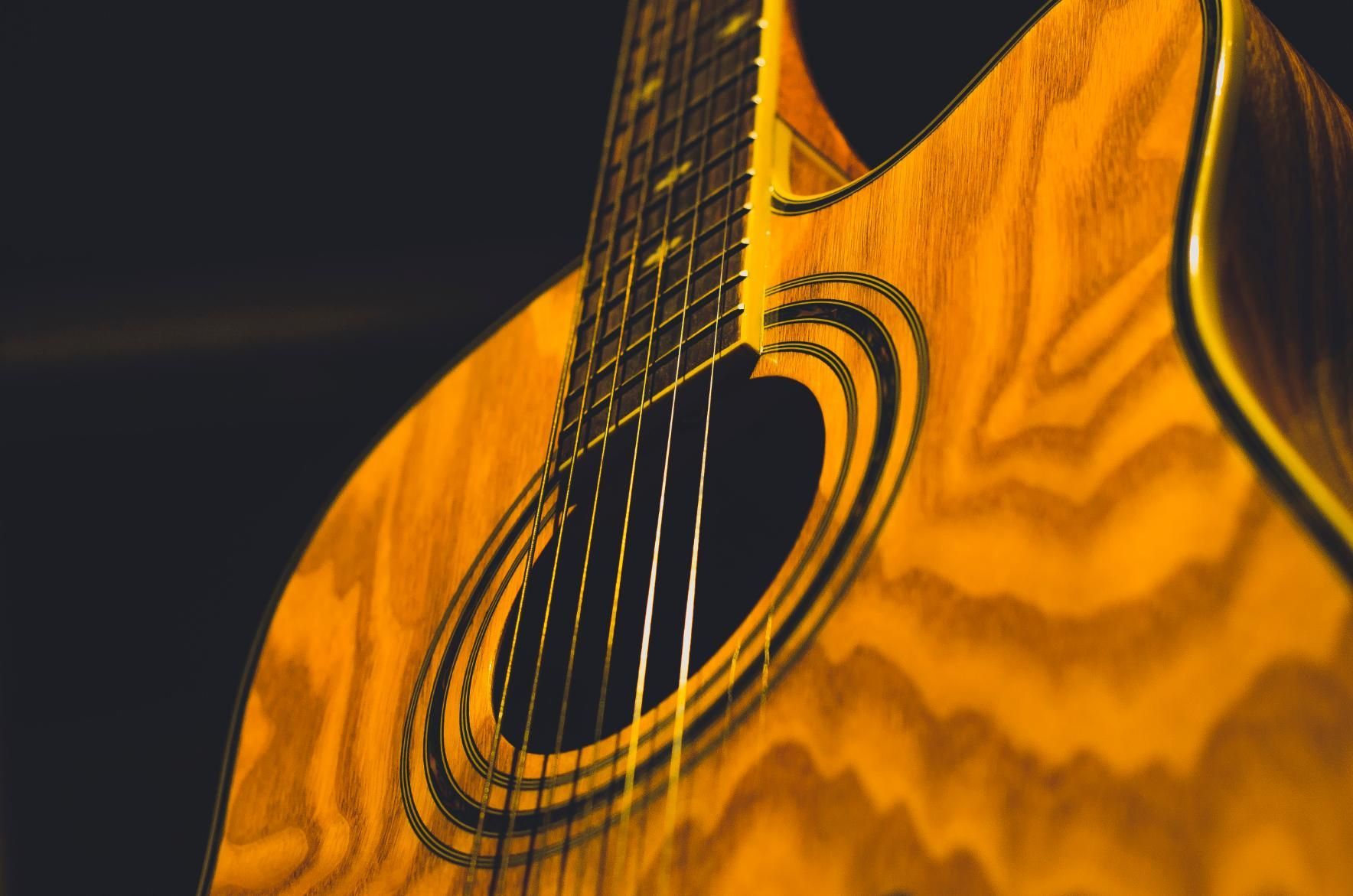 Close-up of a wooden acoustic guitar with a glossy amber finish and circular sound hole against a dark background