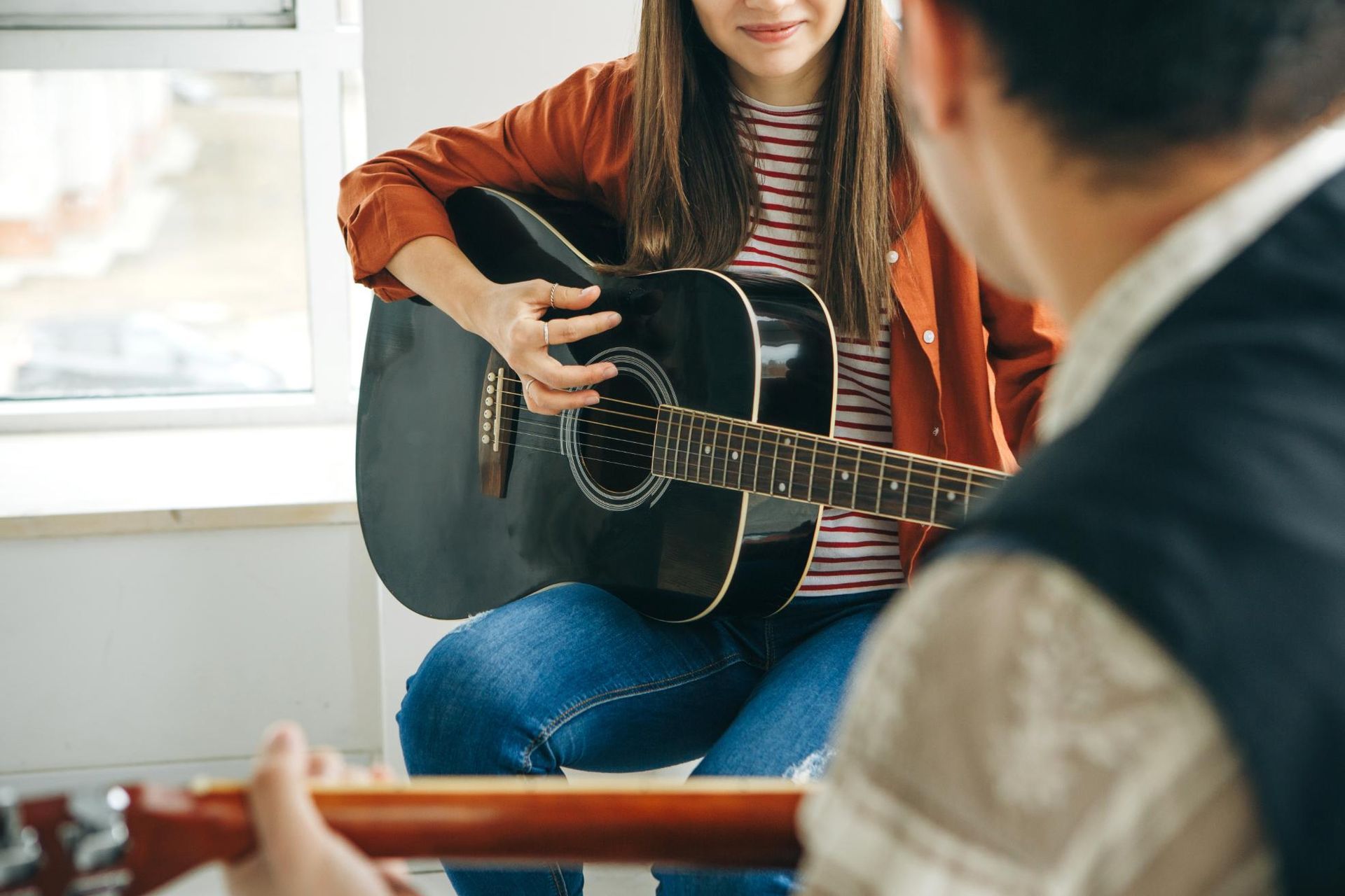 Person holding a black guitar during a music lesson with another guitar in the foreground
