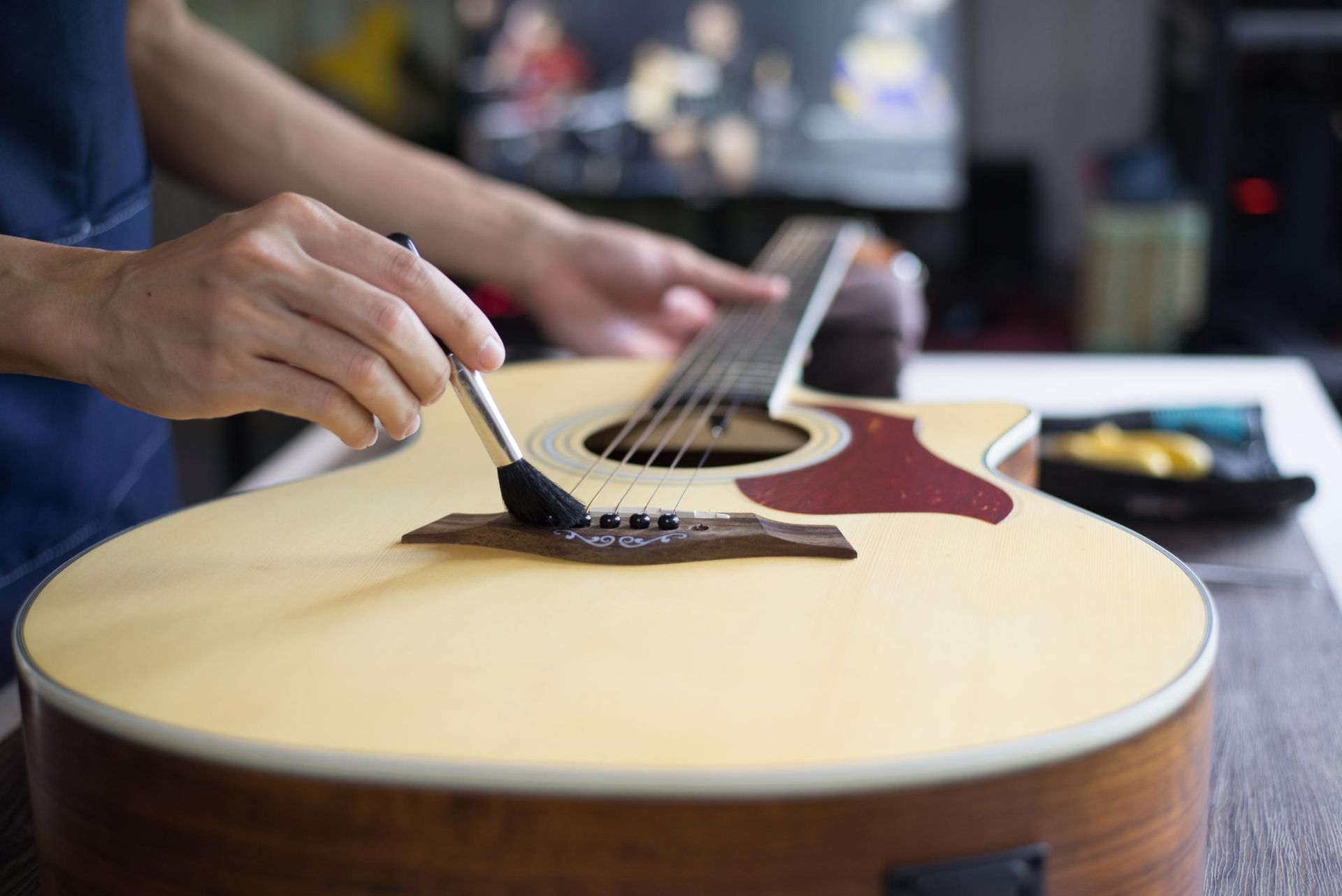 Hands adjusting strings on a light wood acoustic guitar with a red pickguard