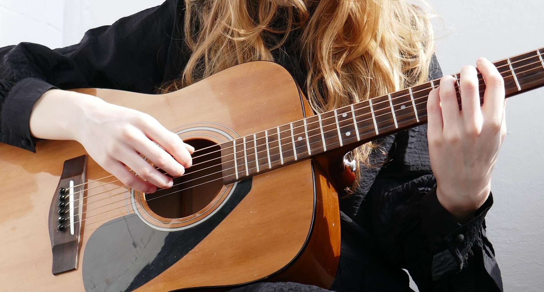 Person playing an acoustic guitar, close-up of hands on the strings and fretboard