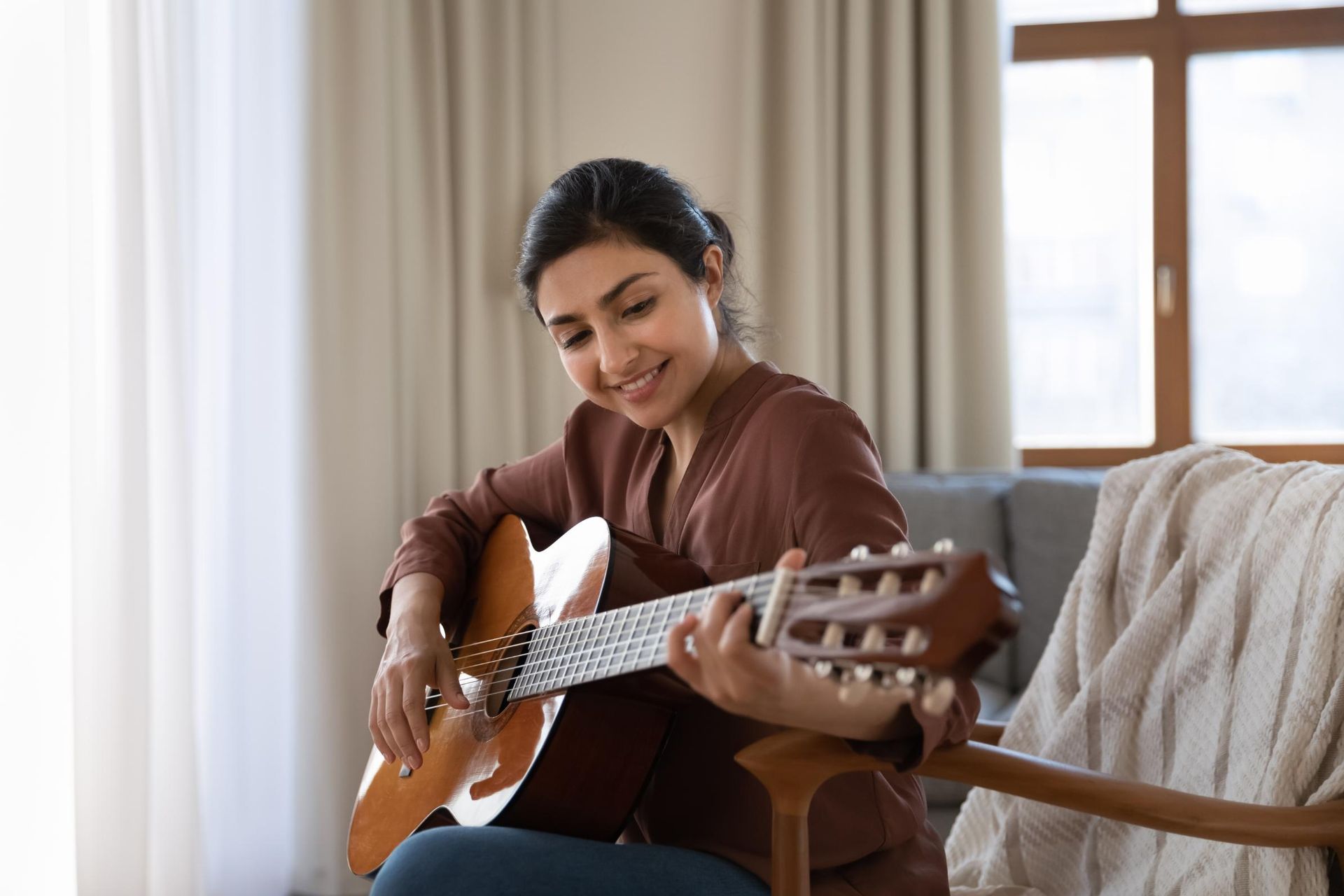 Person playing guitar on a couch in a bright living room