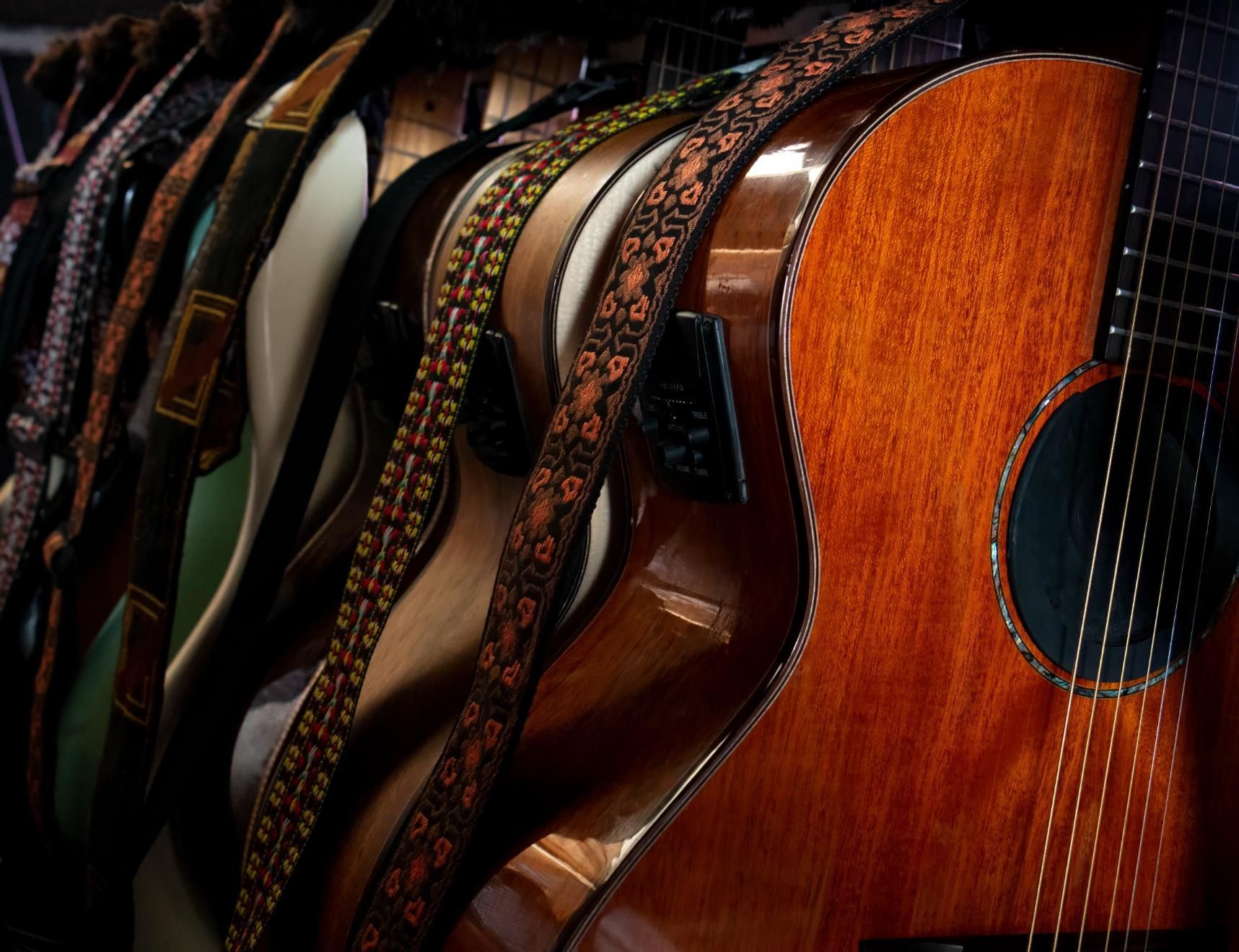 Several wooden acoustic guitars lined up with patterned straps, shown close-up