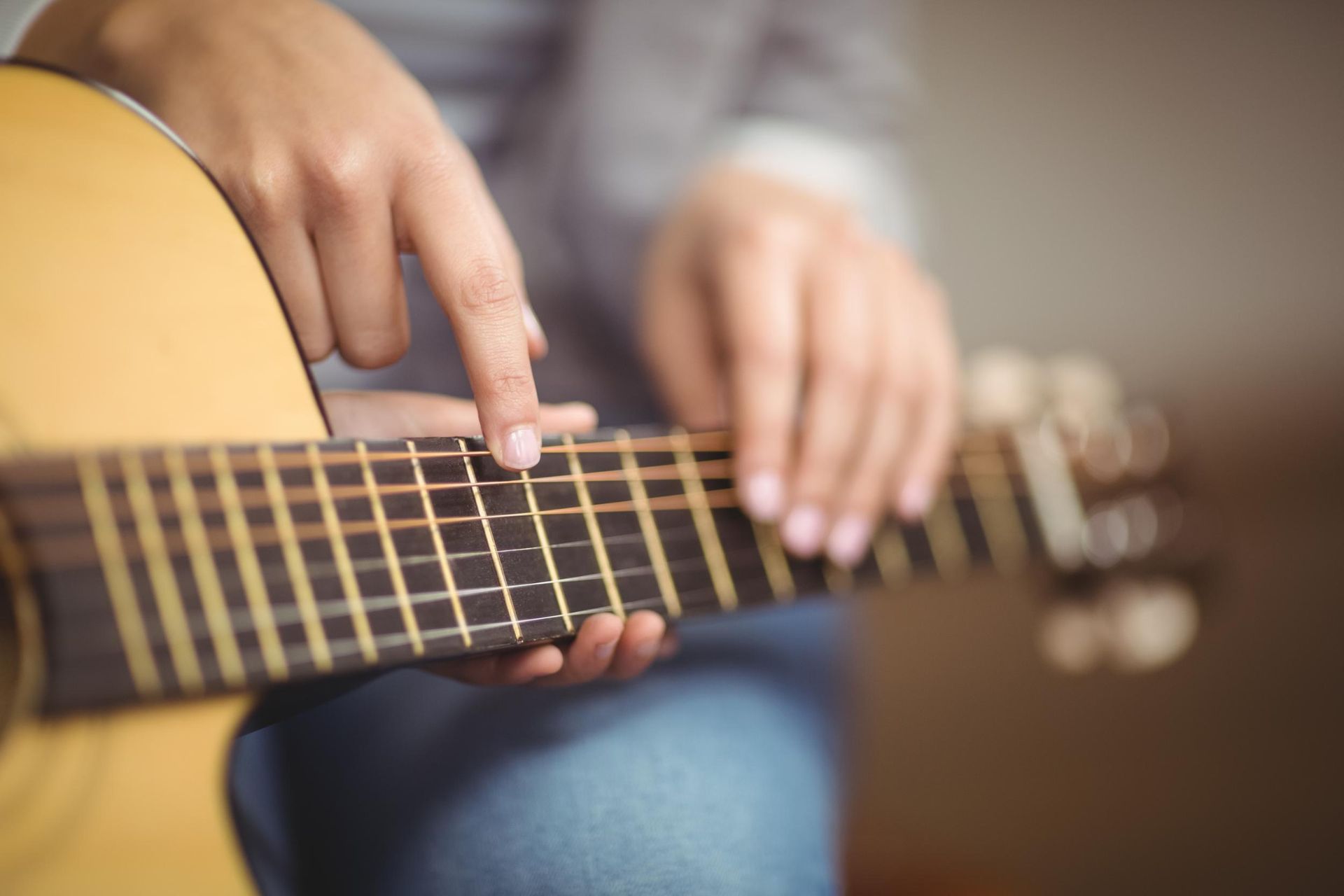 Hands playing a tan acoustic guitar close-up, with fingers on the fretboard.