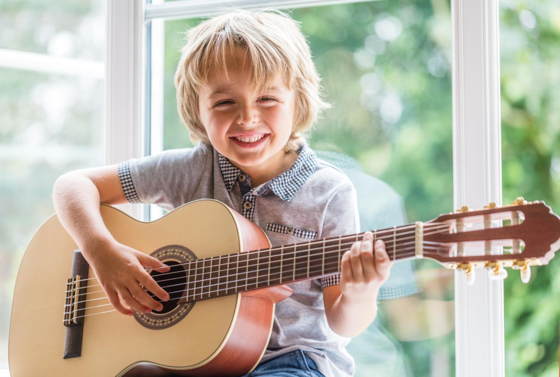 Smiling child playing an acoustic guitar by a bright window