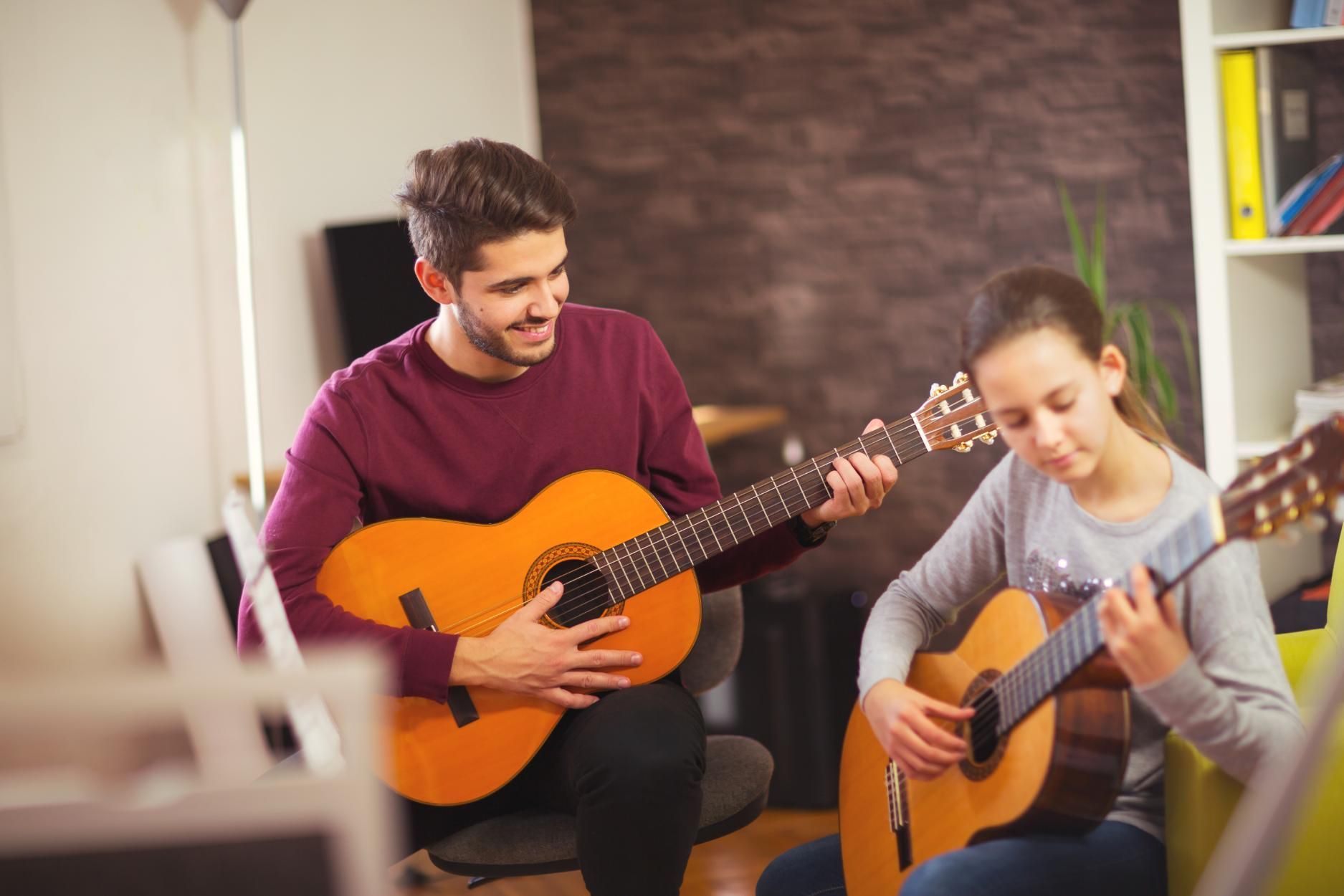Two people playing acoustic guitars together in a cozy indoor room