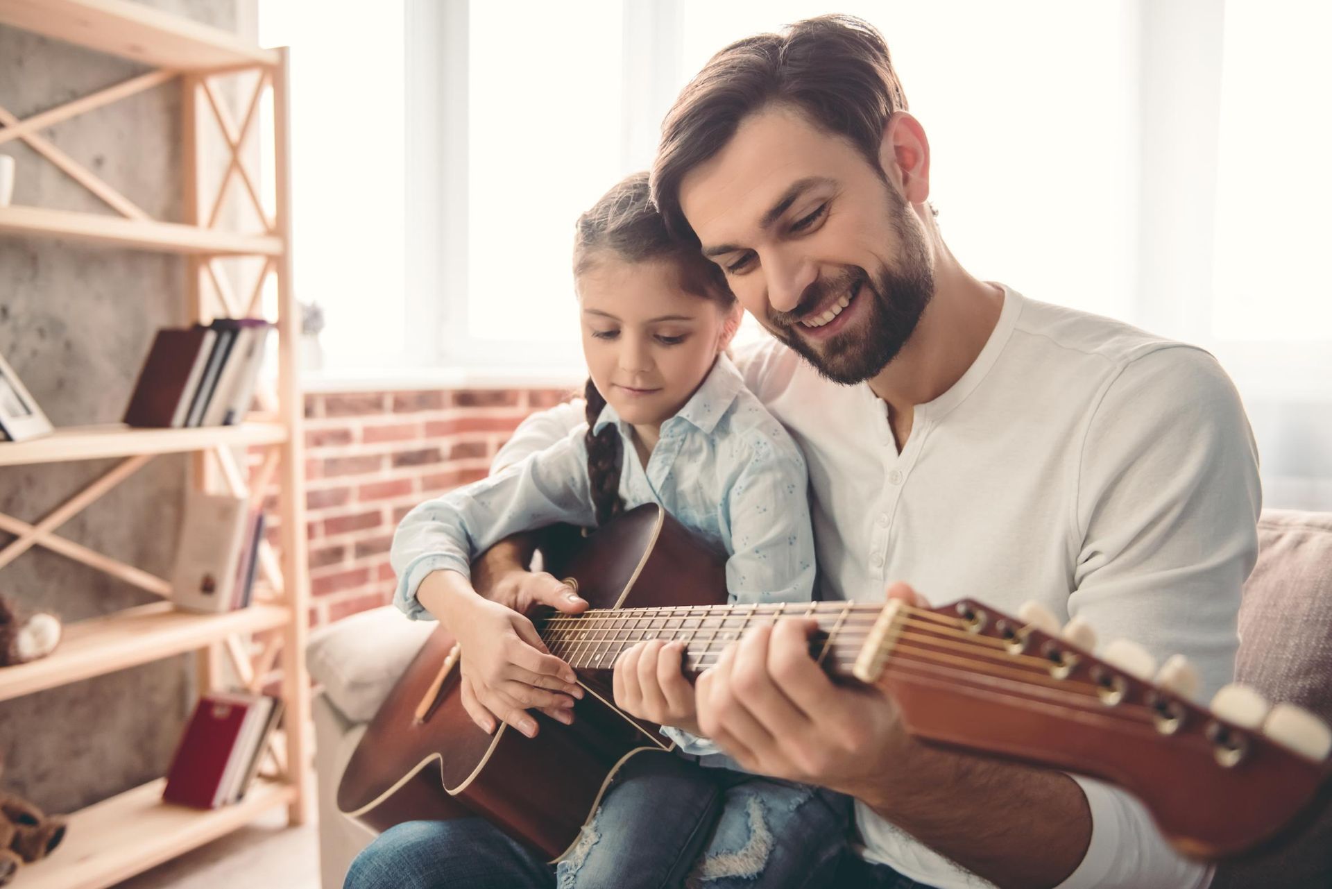 Man and child smiling and playing guitar together in a bright living room
