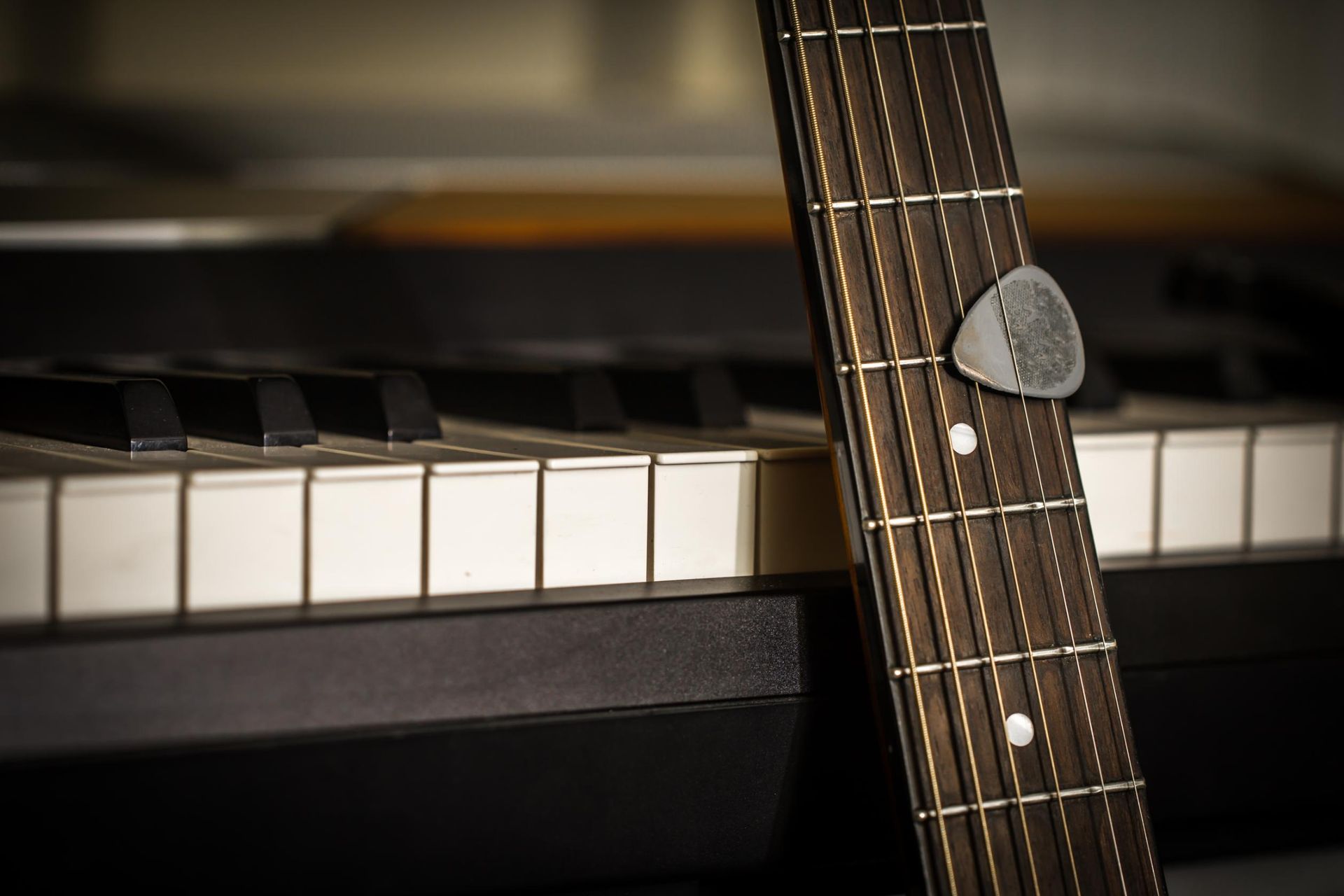 Close-up of a guitar leaning against piano keys, with a gray pick on the fretboard