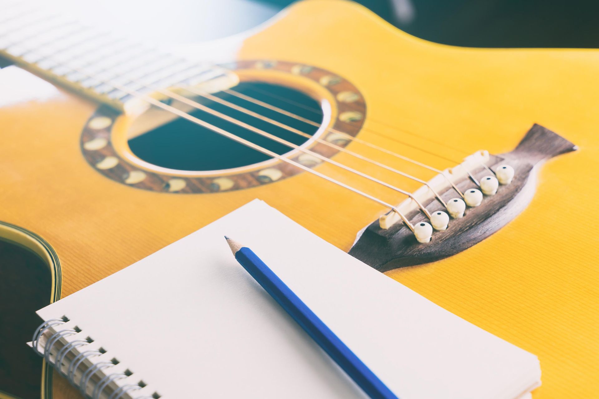 Notebook and blue pencil on a yellow acoustic guitar