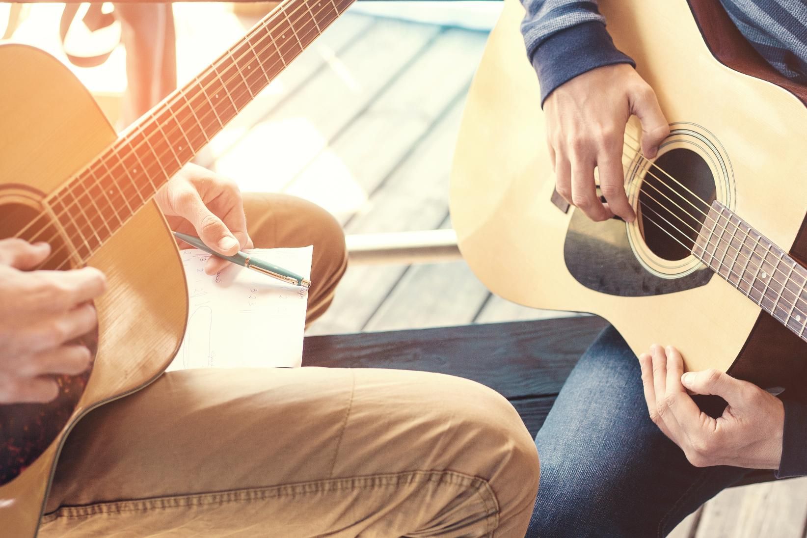 Two people playing acoustic guitars in a sunlit room