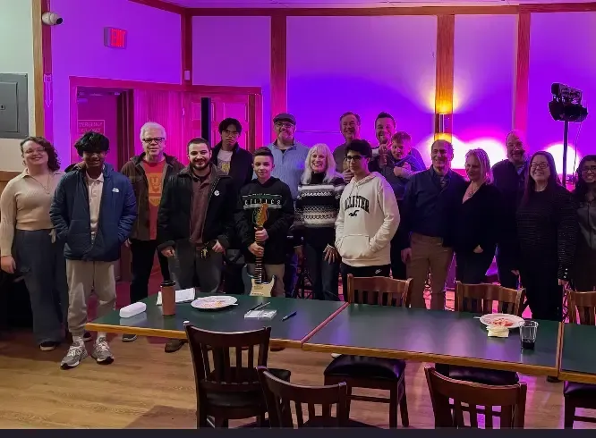 Group of people posing in a hall with purple lighting, tables, and chairs in the foreground