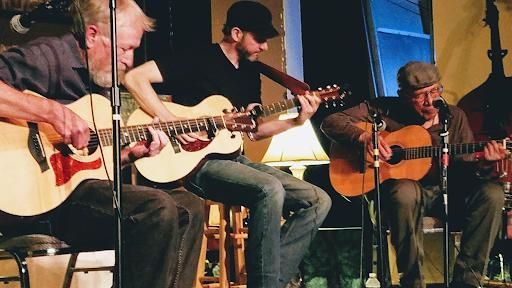 Four musicians seated onstage playing acoustic guitars under warm lighting