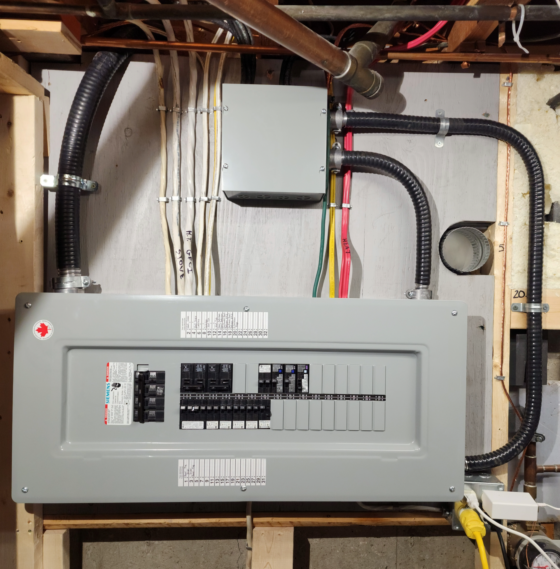Electrical breaker panel with exposed wiring and conduit mounted on a wall in a utility area