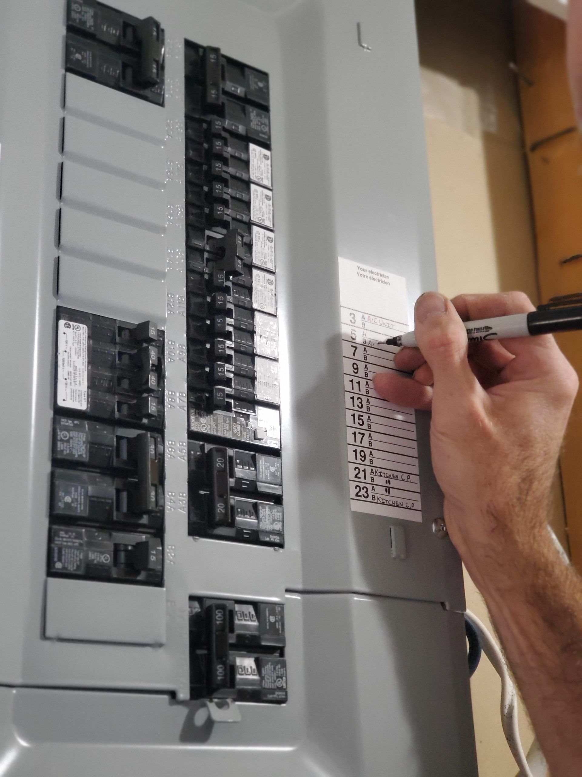Hand placing a label on an electrical breaker panel with switches and circuit breakers visible
