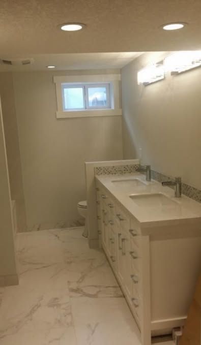 Small bathroom with white vanity, marble floor, recessed lights, and a window at the back.