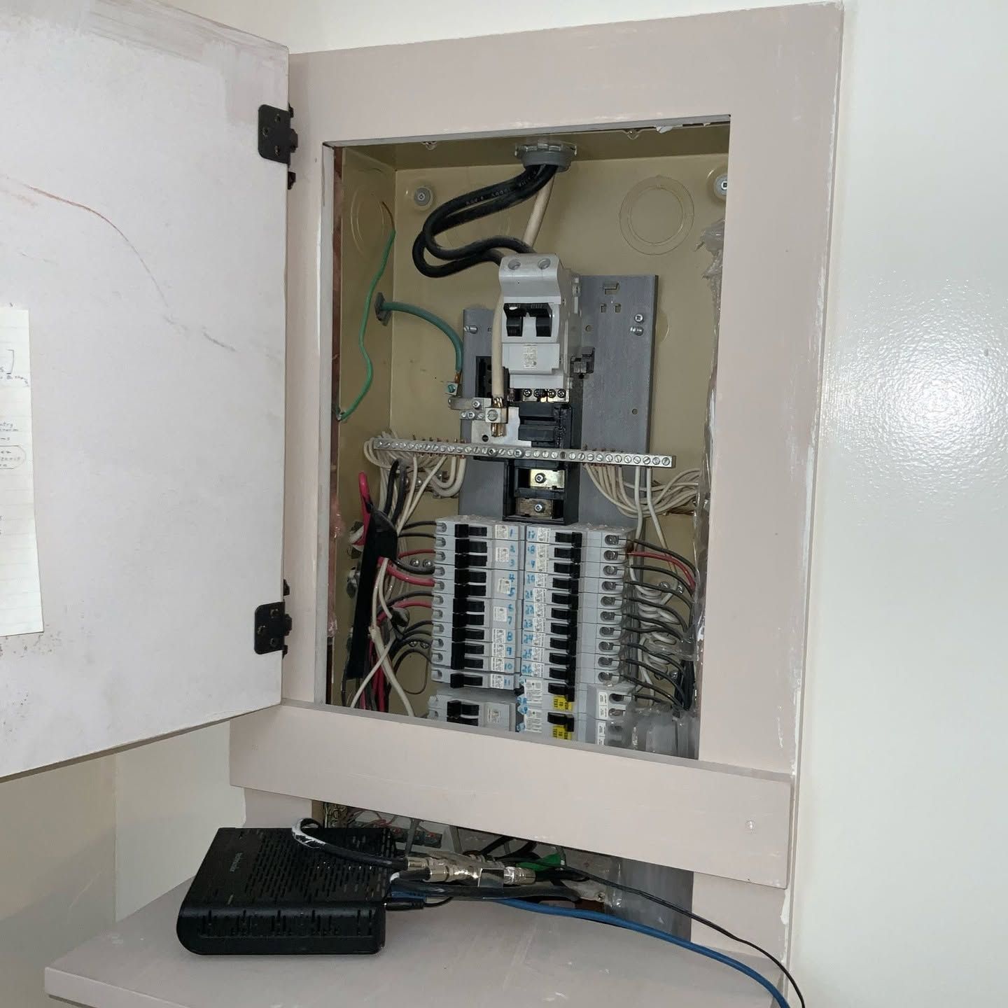 Open electrical breaker panel in a white wall cabinet, with exposed wiring and switches.