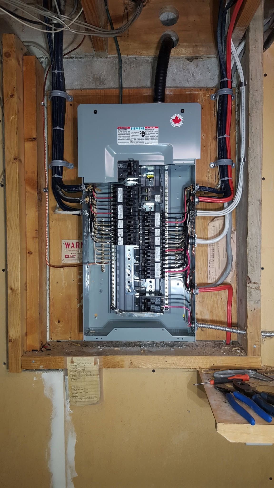 Electrical panel with breakers exposed in an unfinished wall cavity, with visible wiring and conduit.