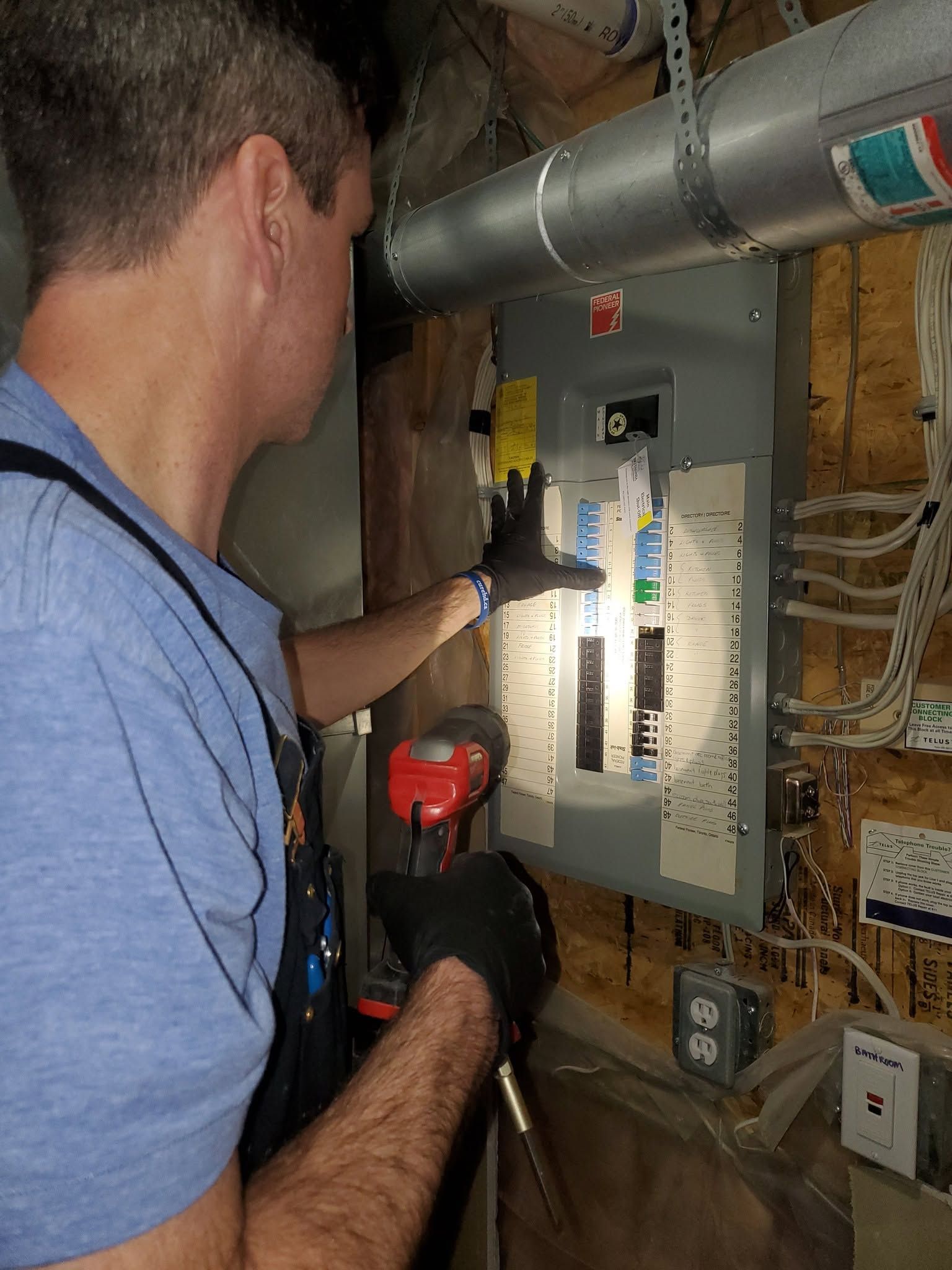 Technician inspecting an electrical panel in a utility room with exposed pipes and wiring.
