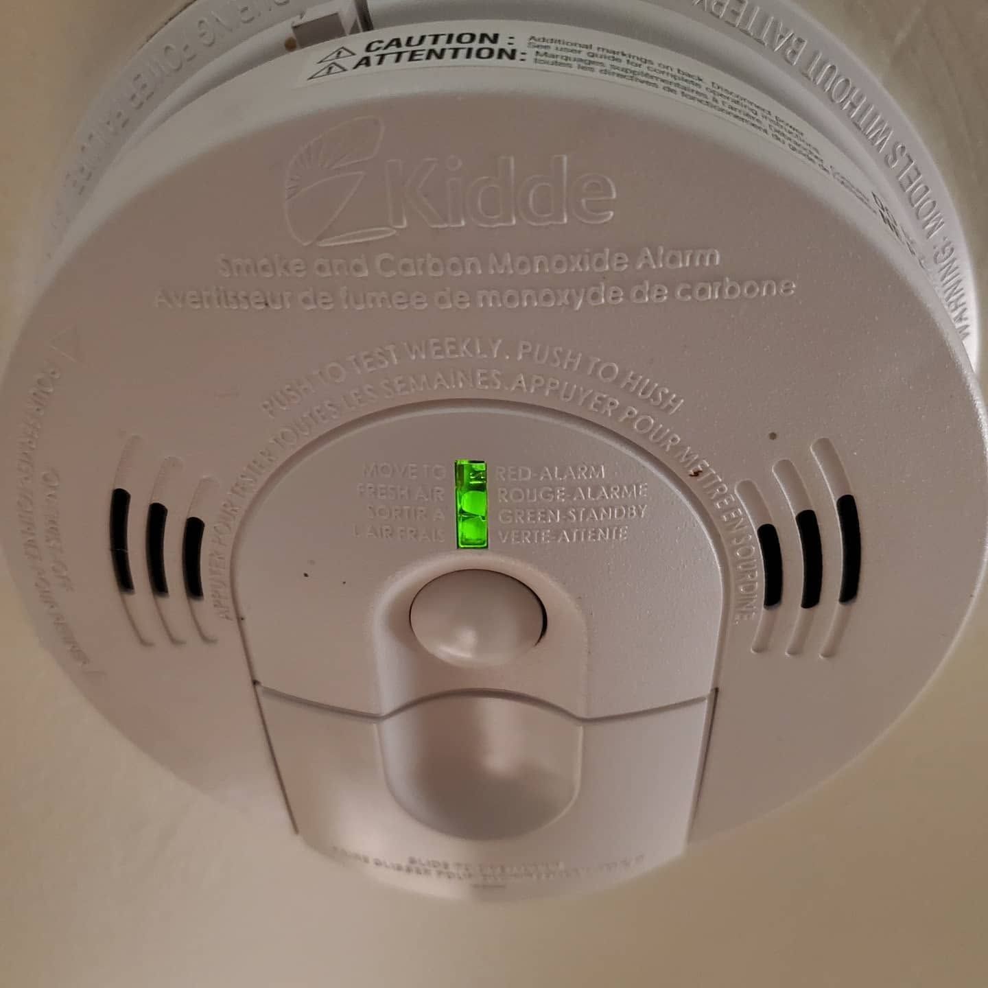 White Kidde smoke and carbon monoxide alarm with green indicator lights and test button on ceiling