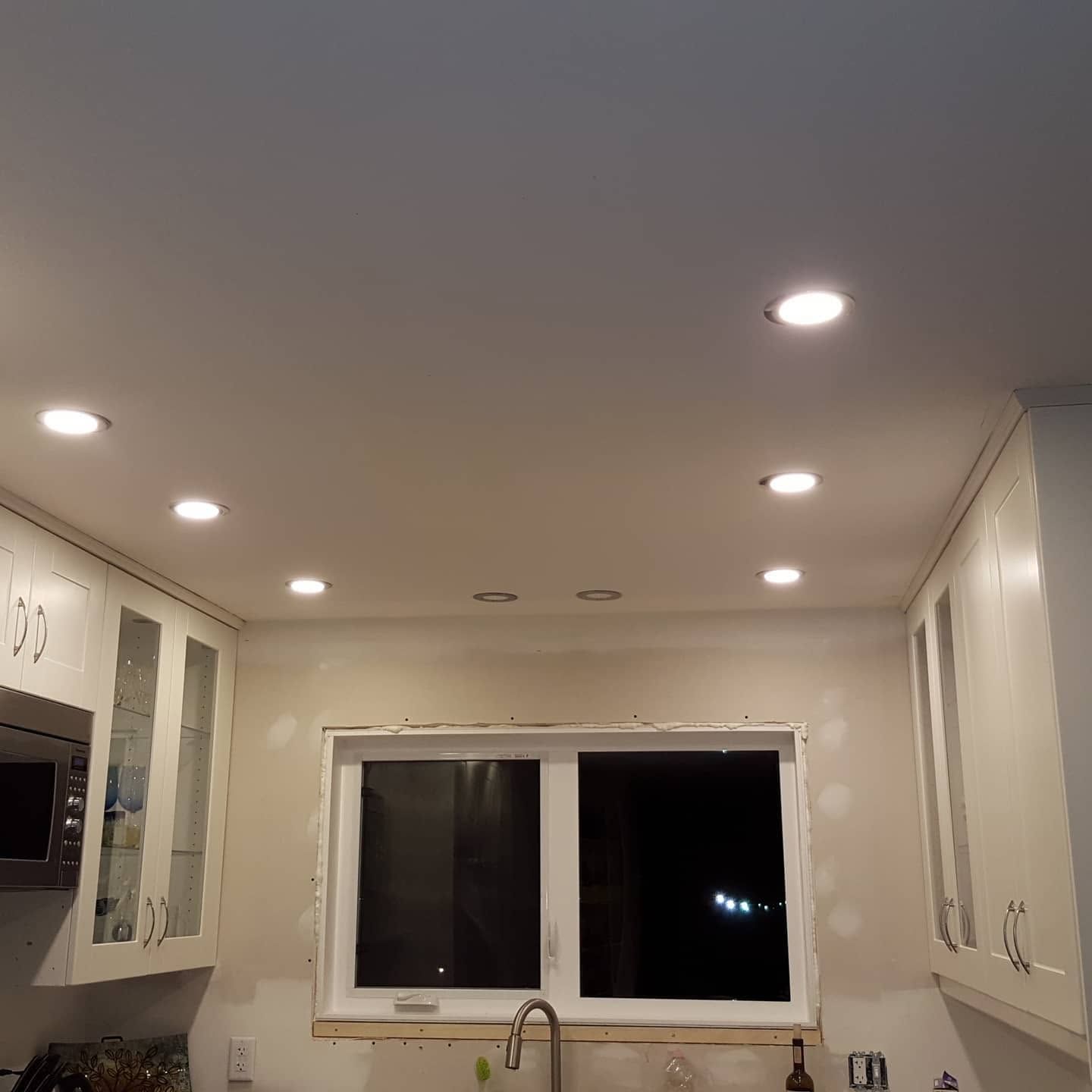 Bright white kitchen ceiling with recessed lights, cabinets, sink, and a window above the counter.