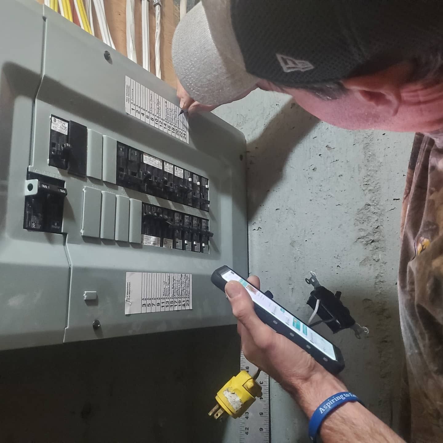 Person inspecting an electrical breaker panel while holding a phone, with a flashlight nearby.