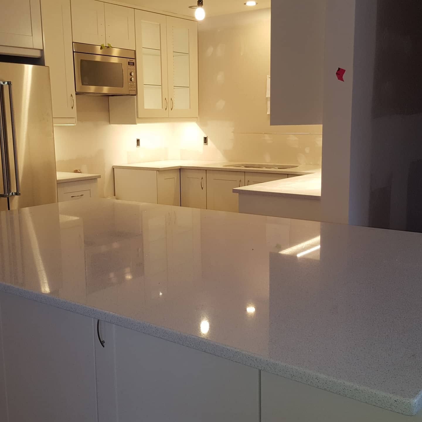 Modern white kitchen with glossy countertops, stainless steel appliances, and warm under-cabinet lighting