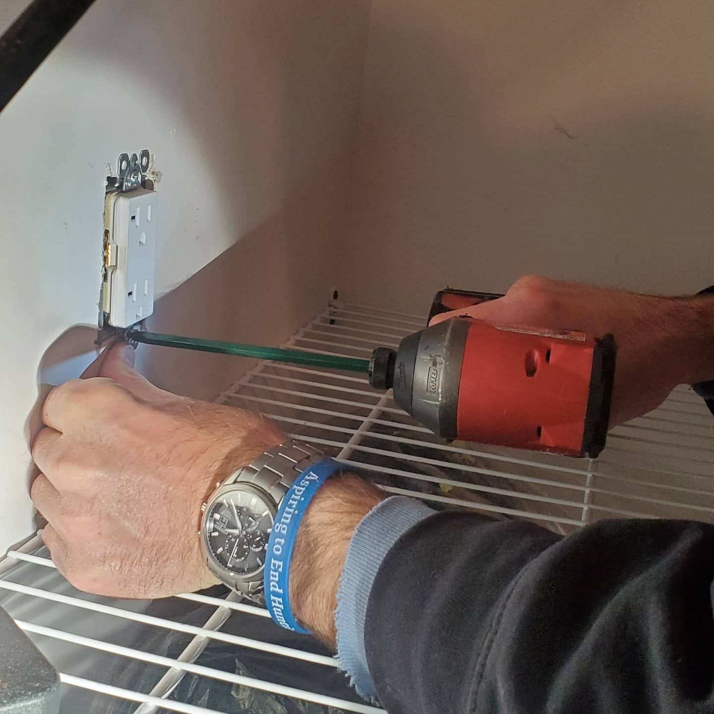Person using a red drill to install a metal shelf bracket on a wall