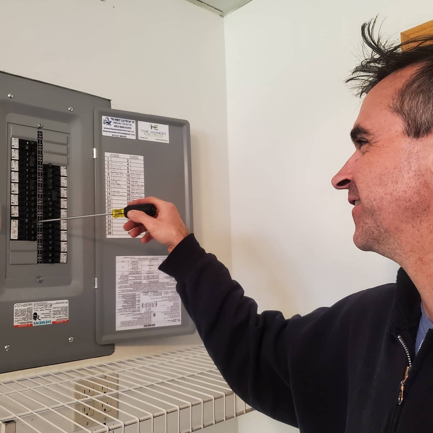 Man turning a circuit breaker in a gray electrical panel indoors