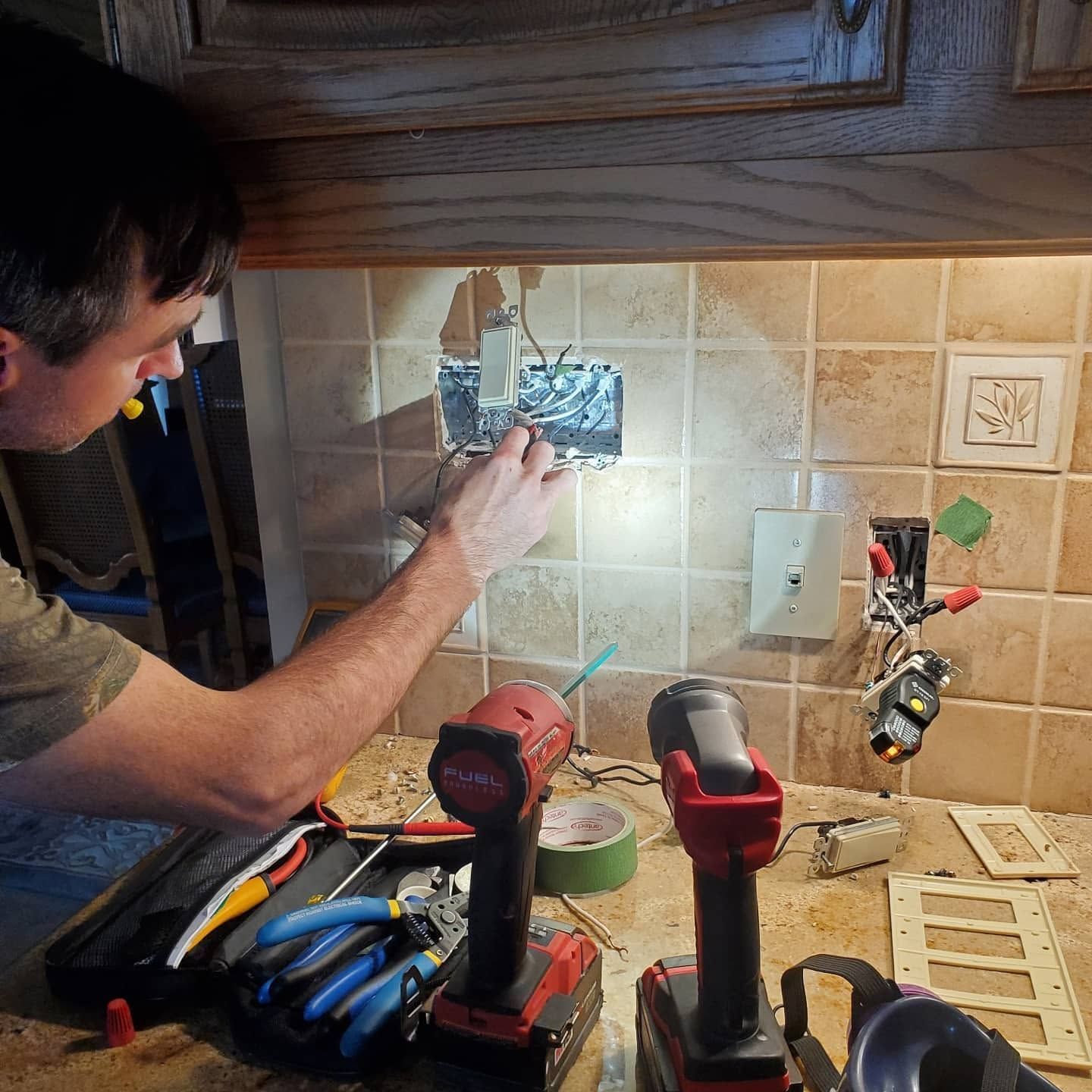 Person wiring an outlet in a tiled kitchen backsplash with tools on the counter.