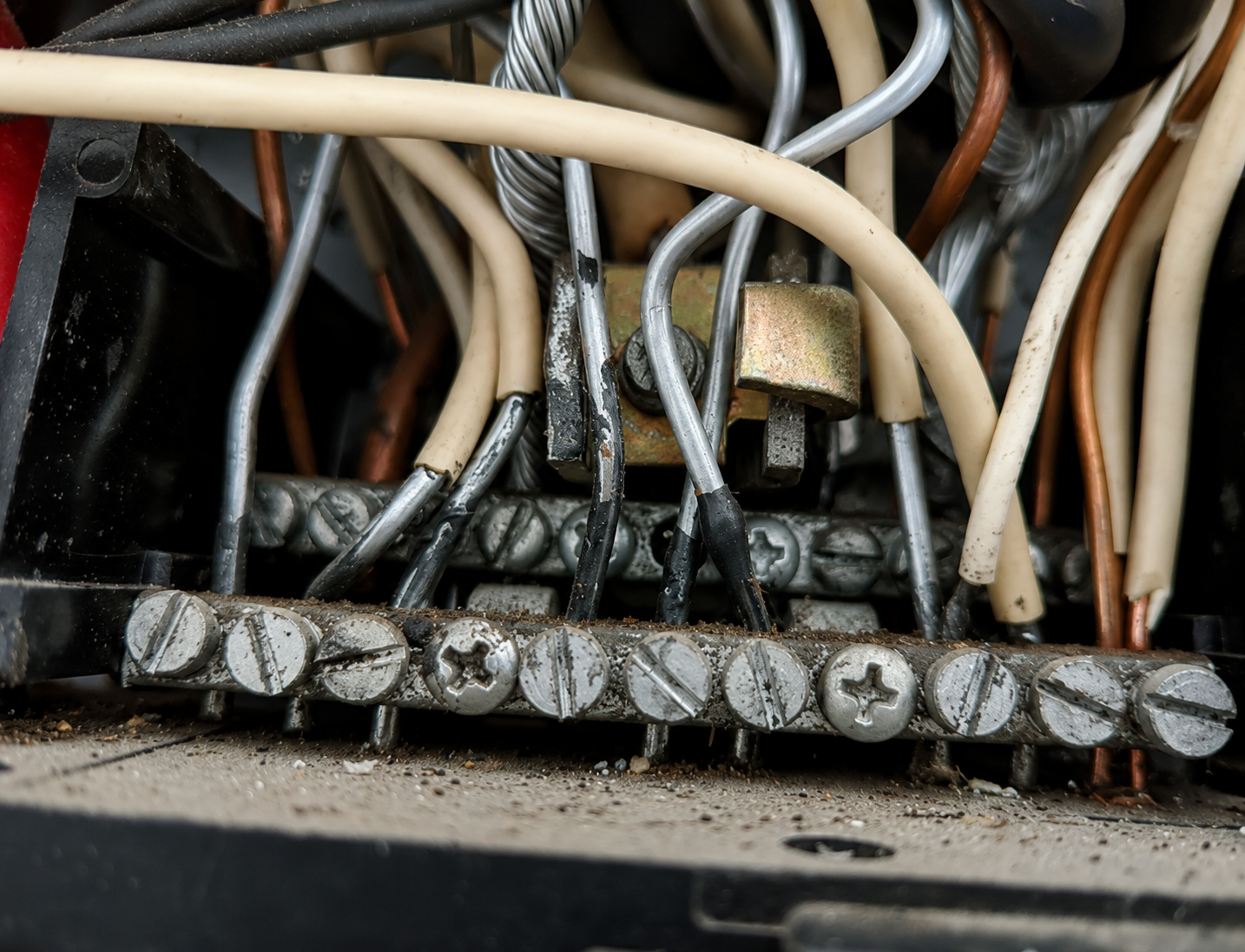 Close-up of a crowded electrical terminal block with many beige and black wires and metal screws