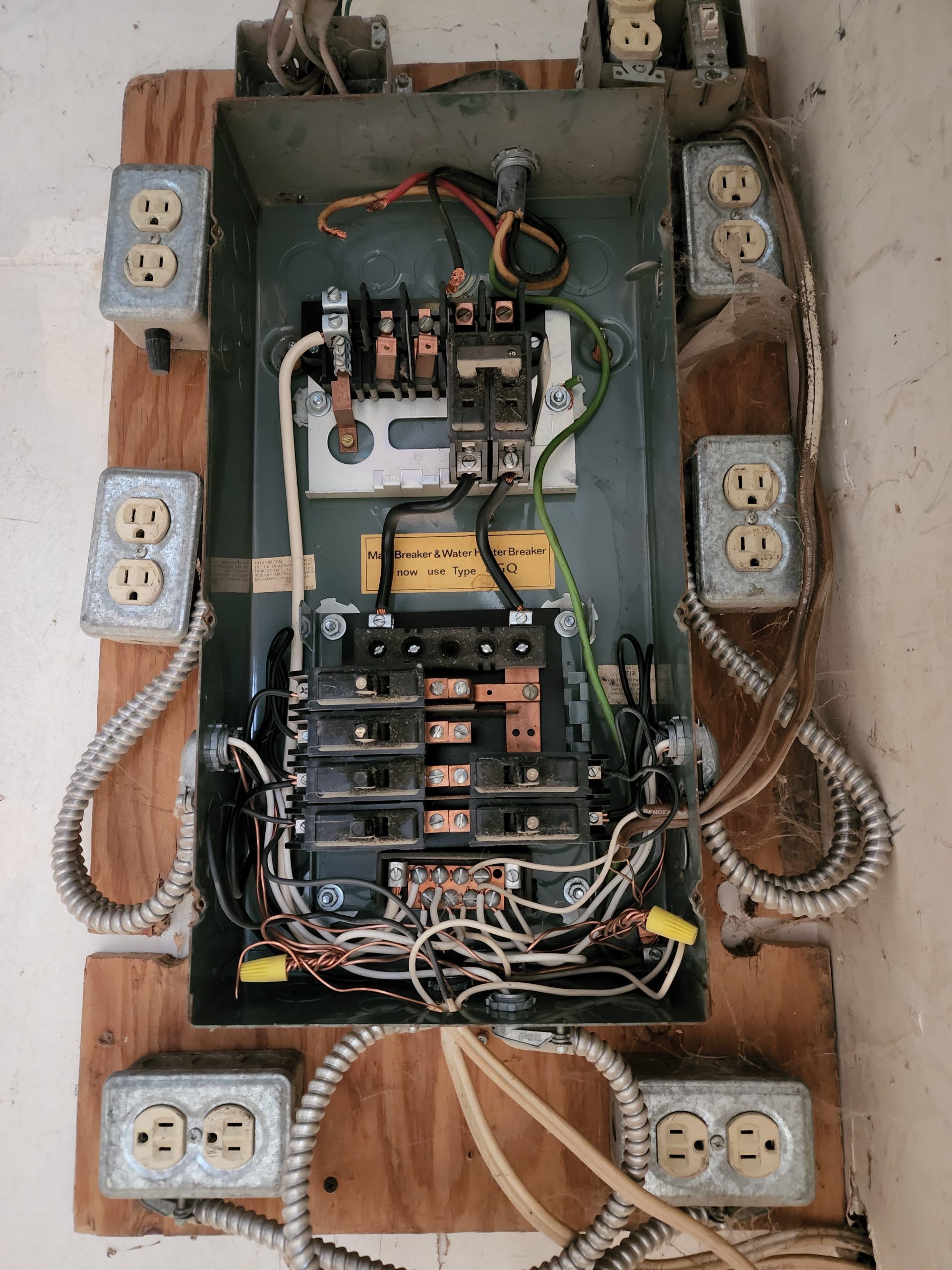 Open electrical breaker panel with exposed wires and multiple outlets mounted on wood.