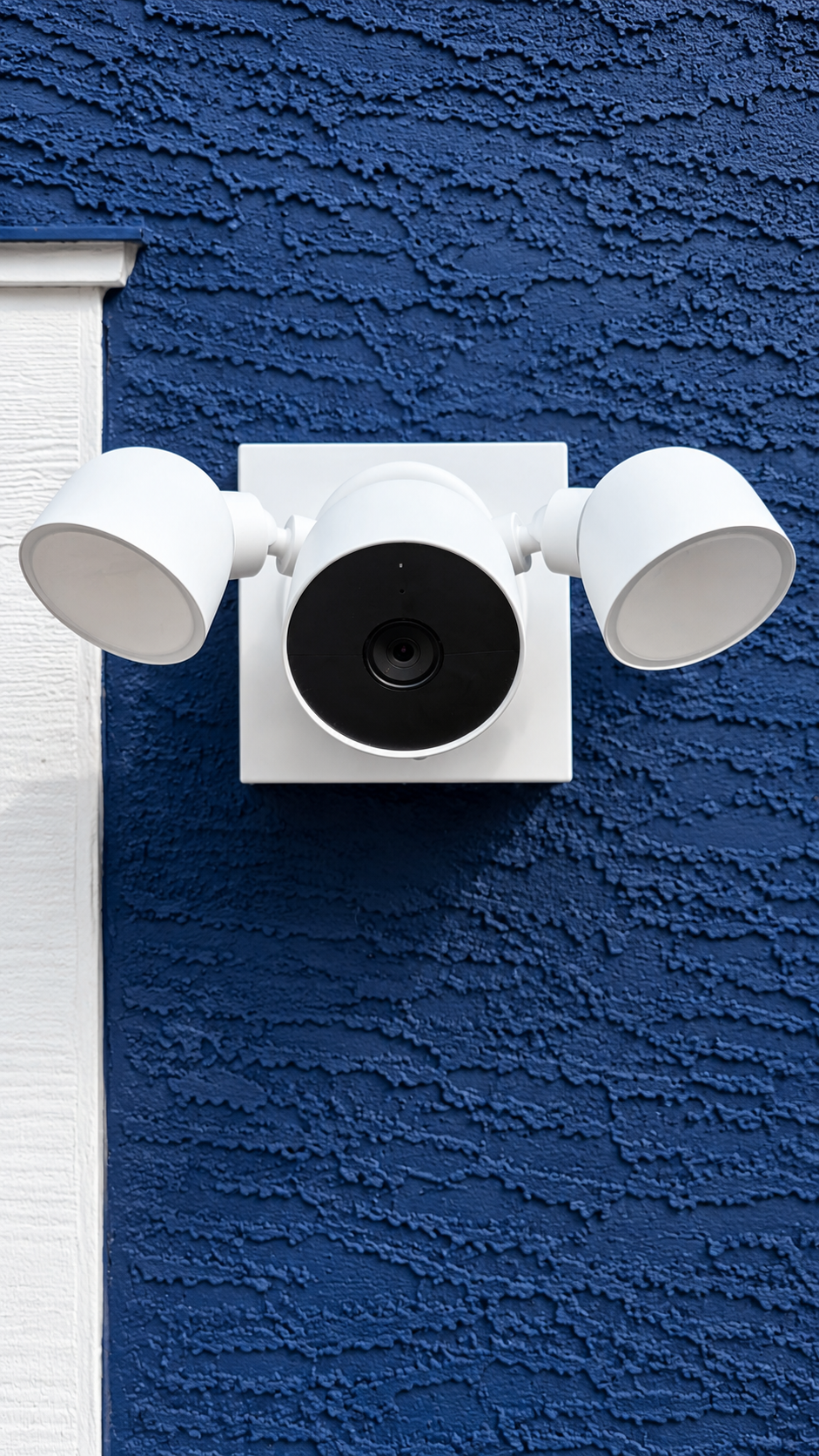 White security camera with two side lights mounted on a blue textured wall