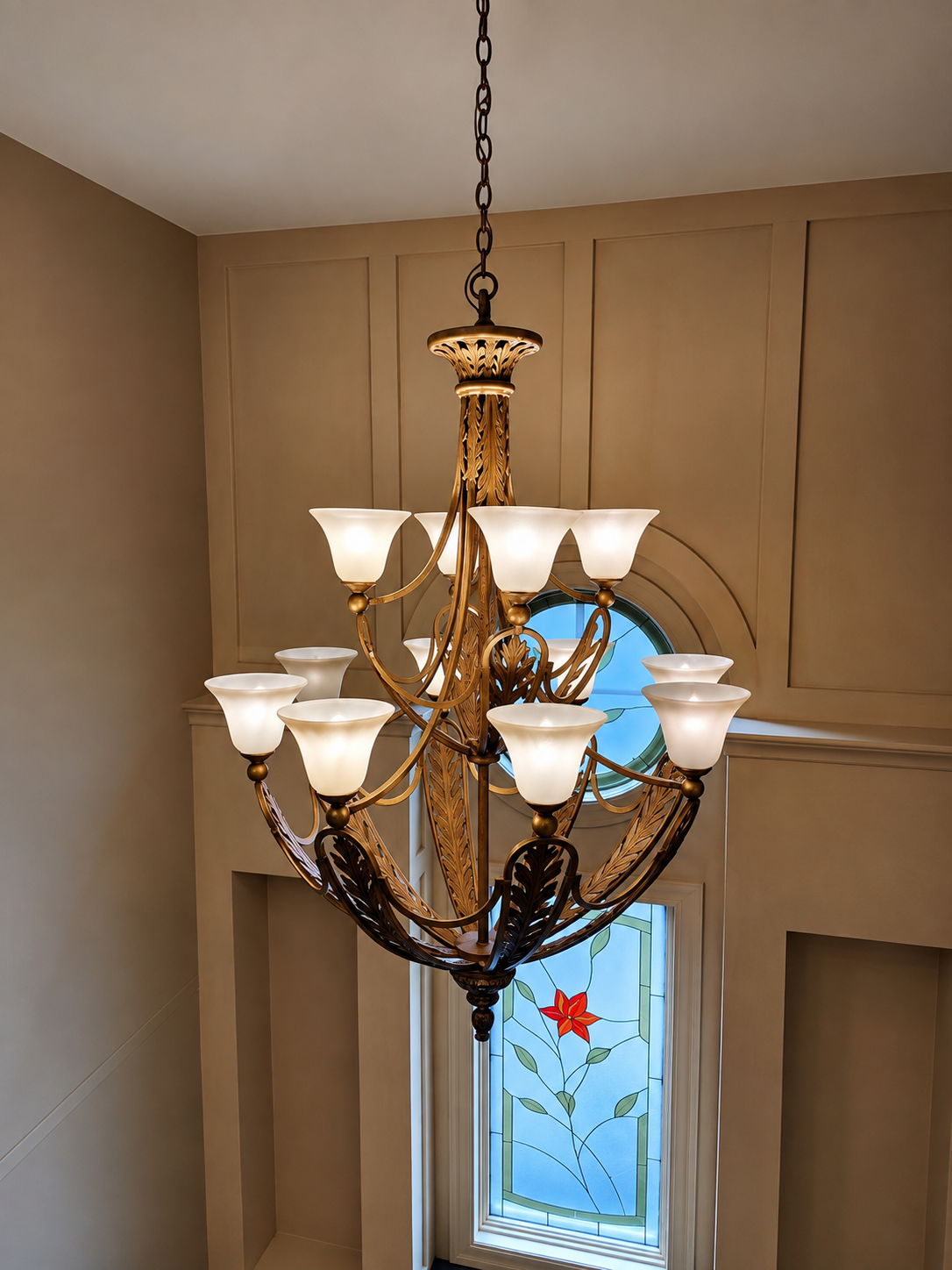 Ornate gold and black chandelier with frosted glass shades hanging in a beige entryway