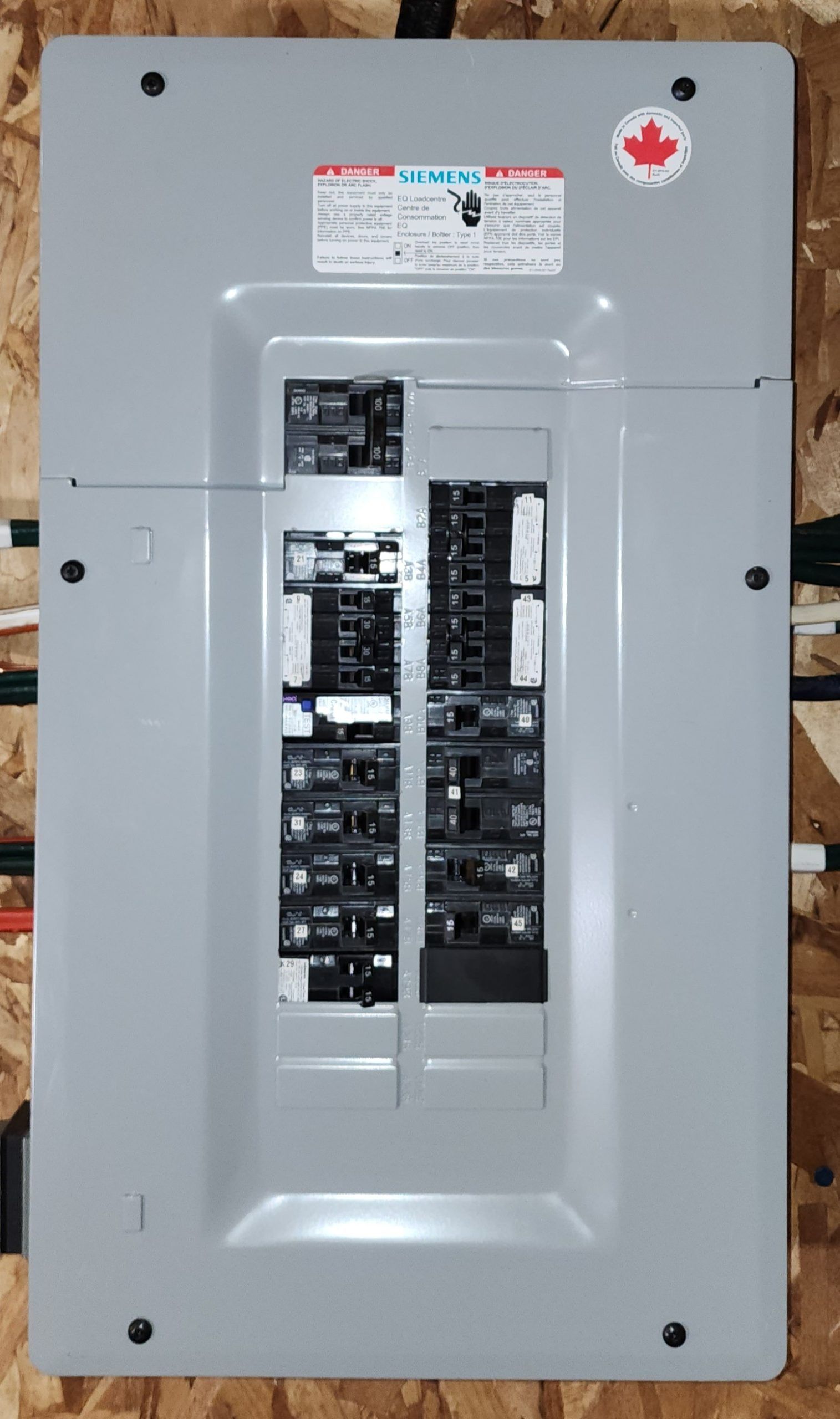 Open electrical breaker panel with gray metal cover and visible circuit breakers on a wall