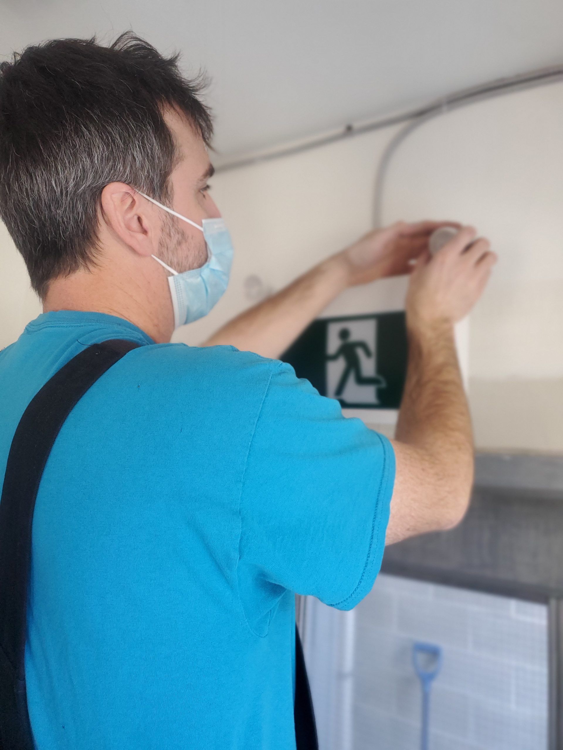 Person in a blue shirt and mask hanging a sign on a wall indoors
