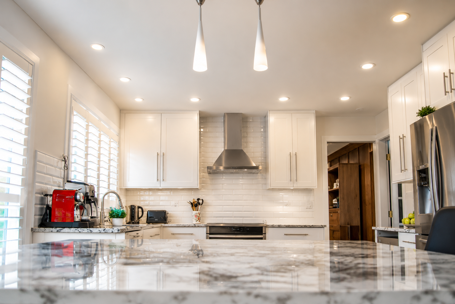 Bright white modern kitchen with marble island, pendant lights, and stainless range hood