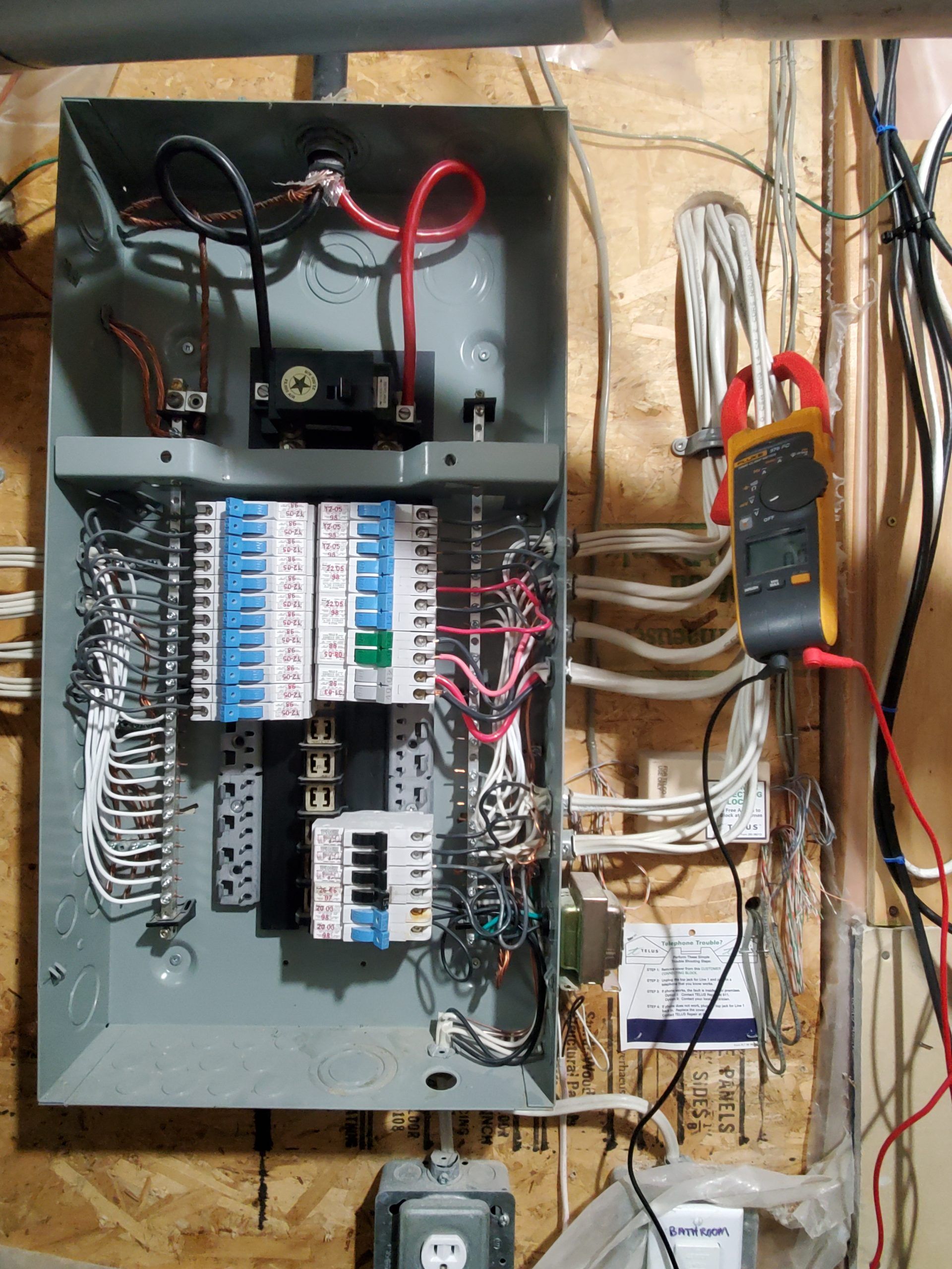 Open electrical breaker panel with wiring and a detached meter on the wall