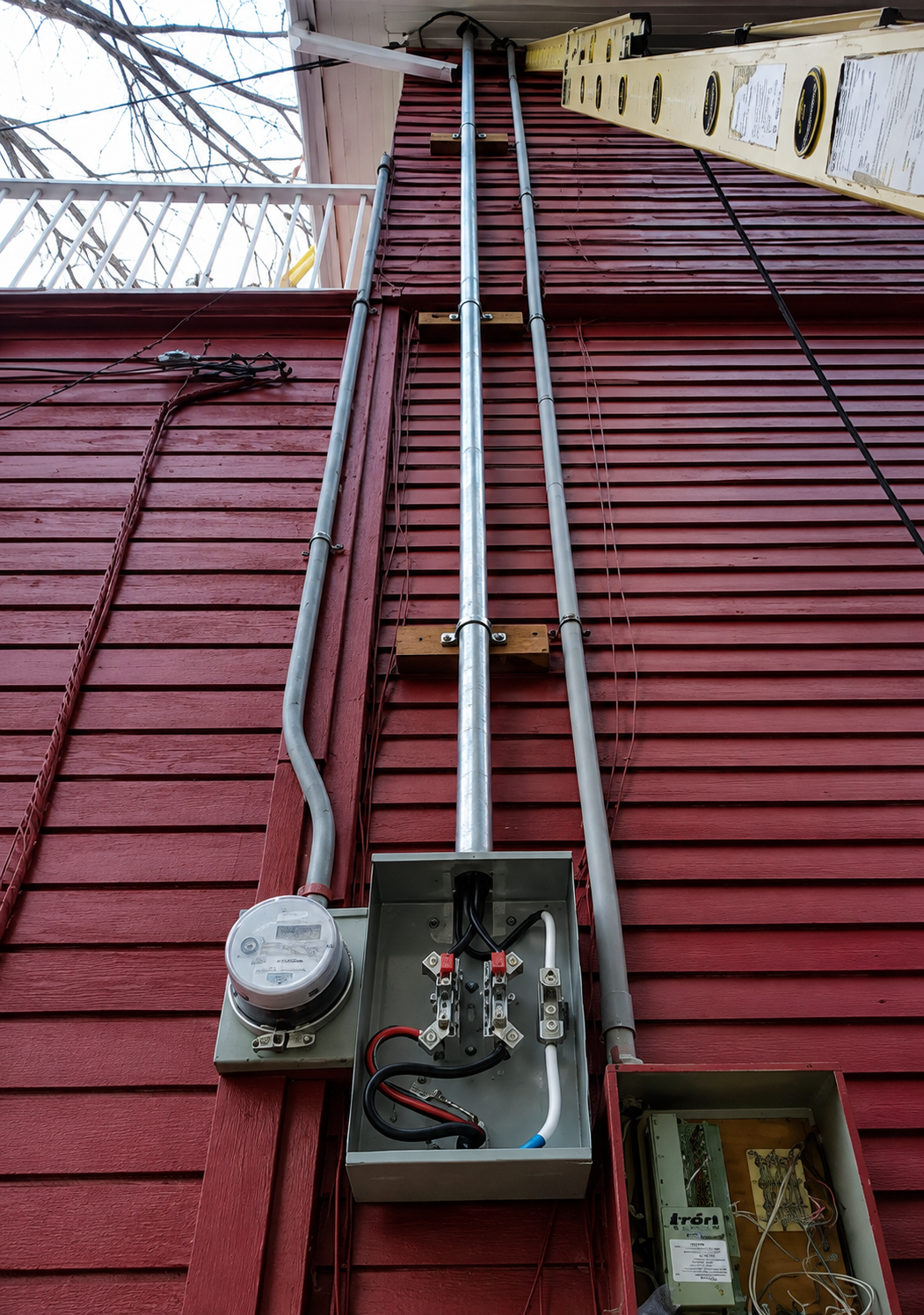 Open electrical meter and conduit on red-sided house exterior under overhang