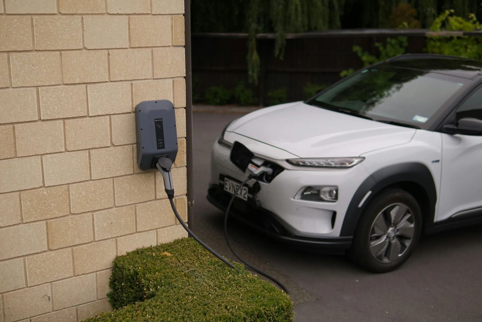White SUV with front-end damage near a wall-mounted EV charger by a brick building