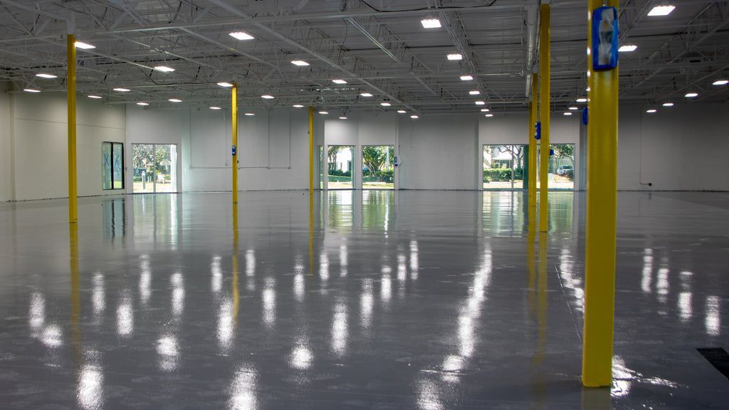 Empty industrial warehouse with polished concrete floor, yellow support columns, and large windows.