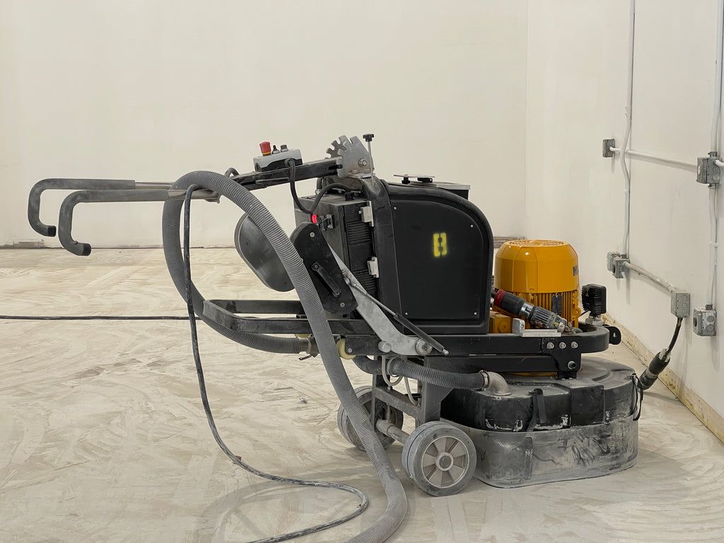Industrial floor-cleaning machine with hoses and wheels on a concrete floor in a white room